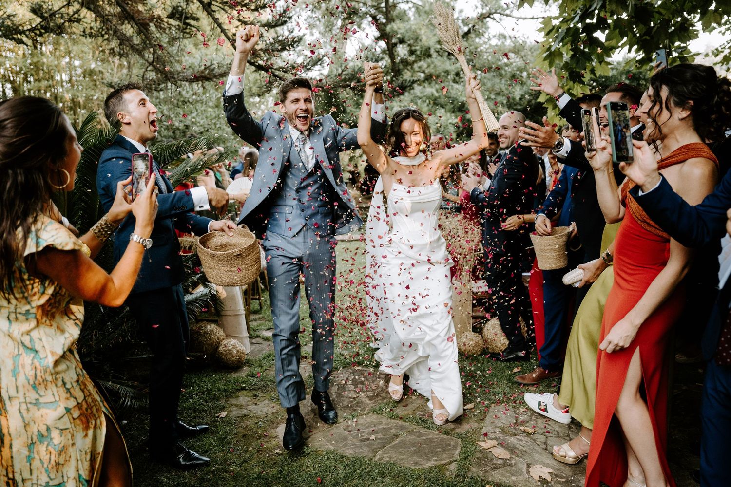 Joyful wedding celebration with guests throwing confetti in an outdoor garden setting.