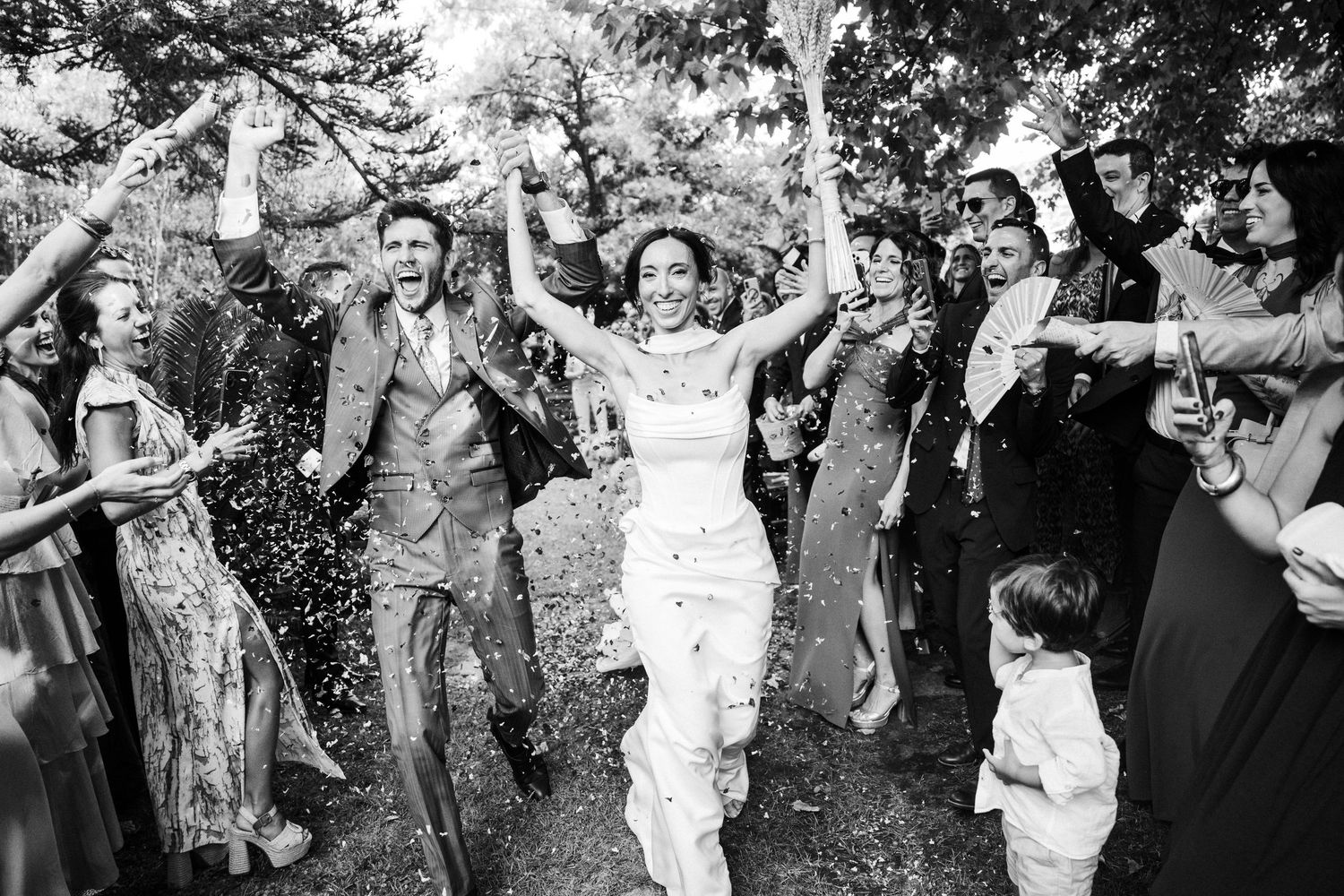 Black and white photo of wedding guests celebrating with confetti outdoors. Jardins El Roquer