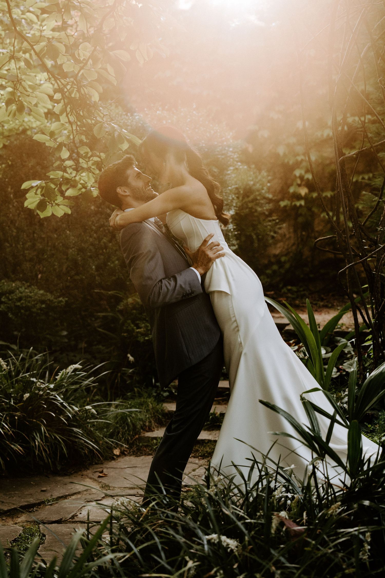 Romantic garden wedding photo with couple embracing in golden sunlight. Jardins el Roquer
