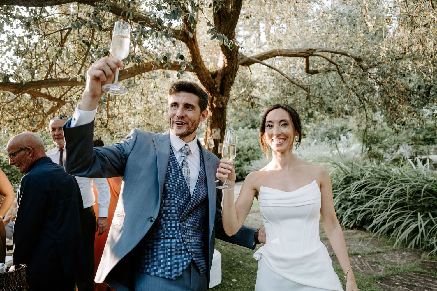 Newlyweds celebrate with raised arms during outdoor wedding reception.