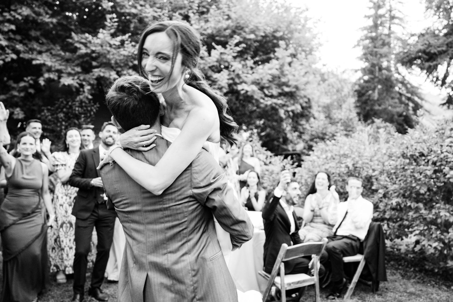 Joyful celebration at an outdoor wedding with guests gathered in a garden setting.