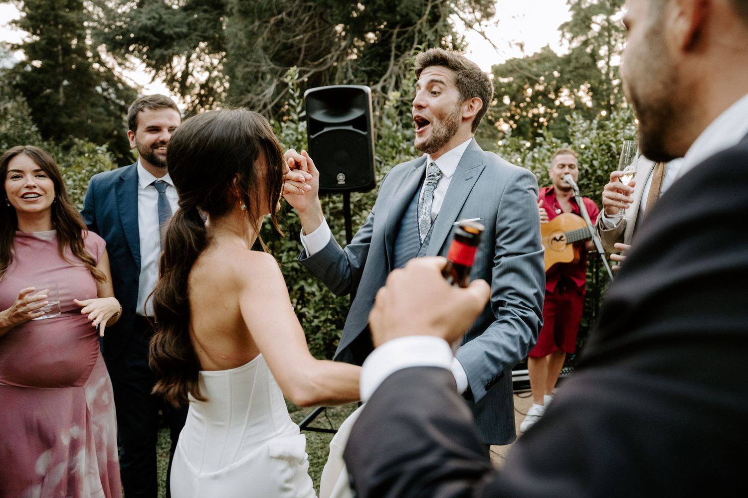Wedding celebration with guests laughing and dancing in an outdoor garden setting.
