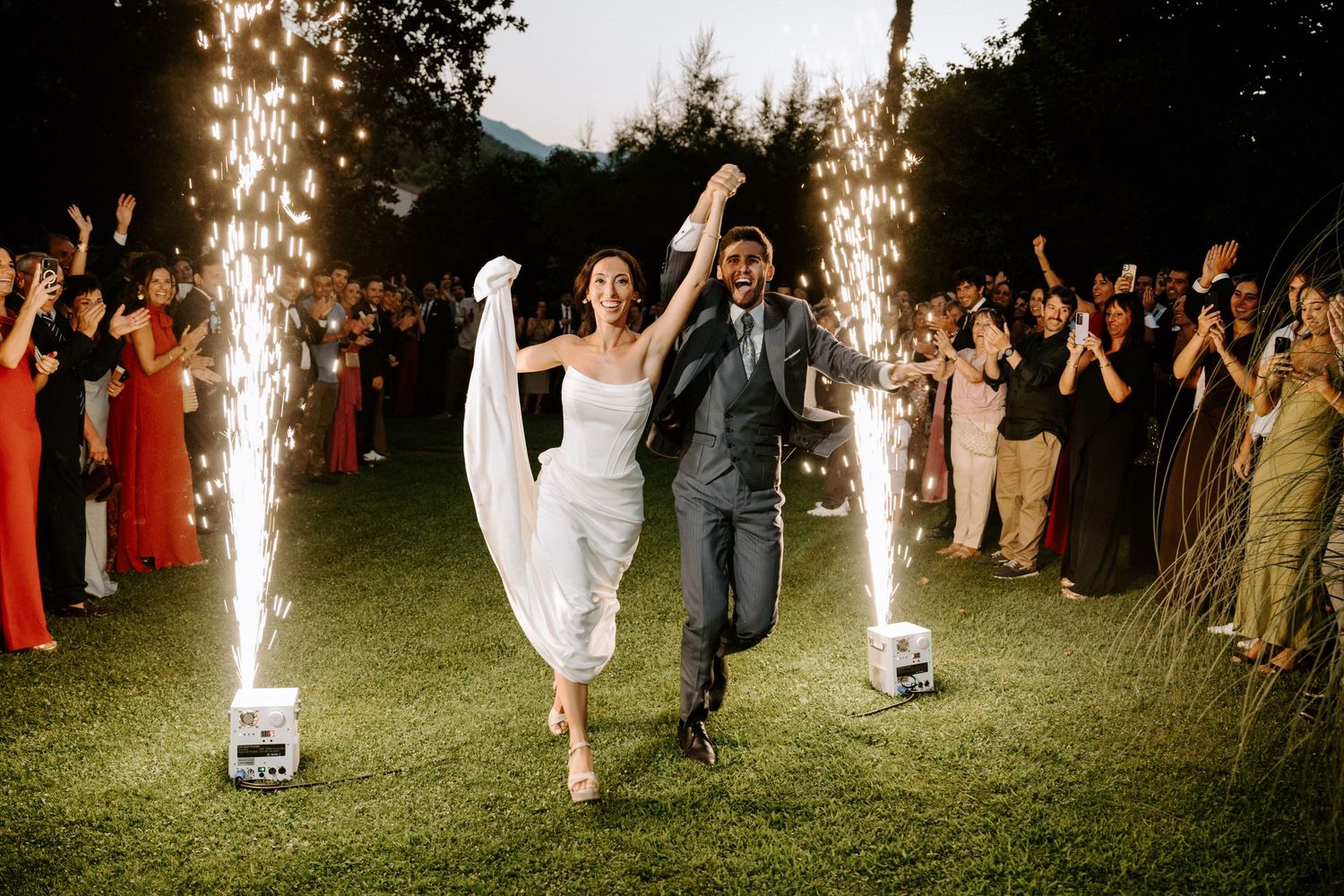Sparklers illuminate an outdoor nighttime wedding celebration on a grassy lawn.