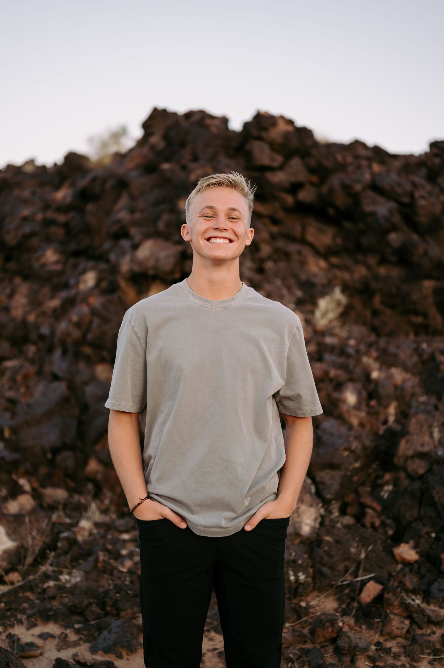 Person in grey t-shirt and dark pants poses against rocky terrain at sunset.