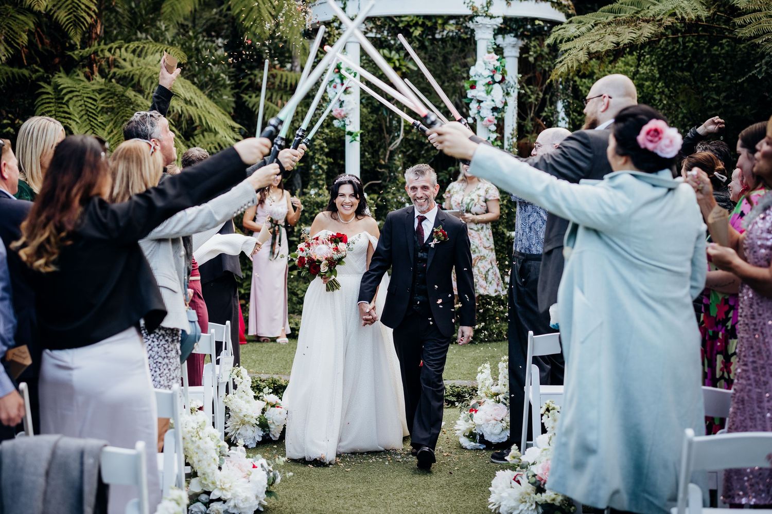 Wedding guests toss colorful confetti in celebration during an outdoor ceremony.