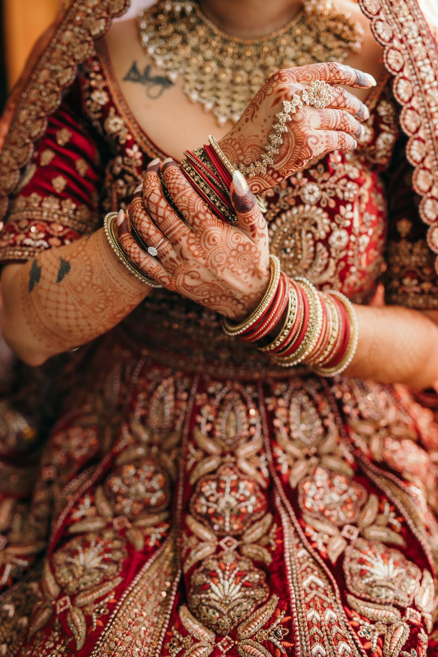 Close-up of bridal hands with intricate henna designs, bangles, and traditional red wedding attire.