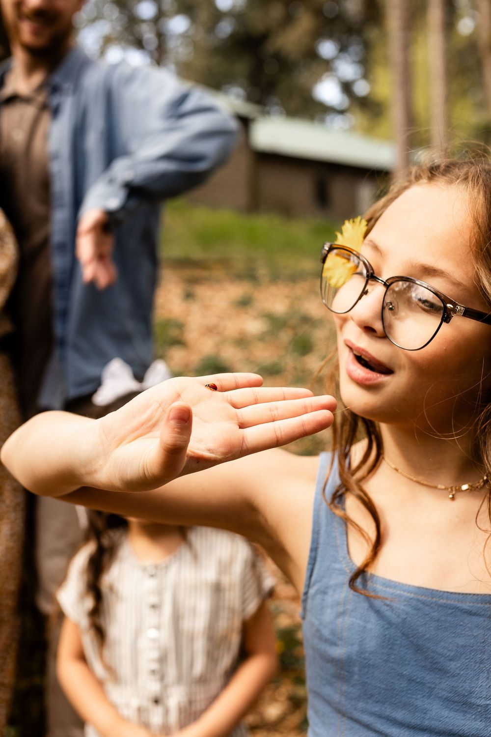 Woman in glasses and blue top poses outdoors with wind blowing through her hair against natural backdrop.