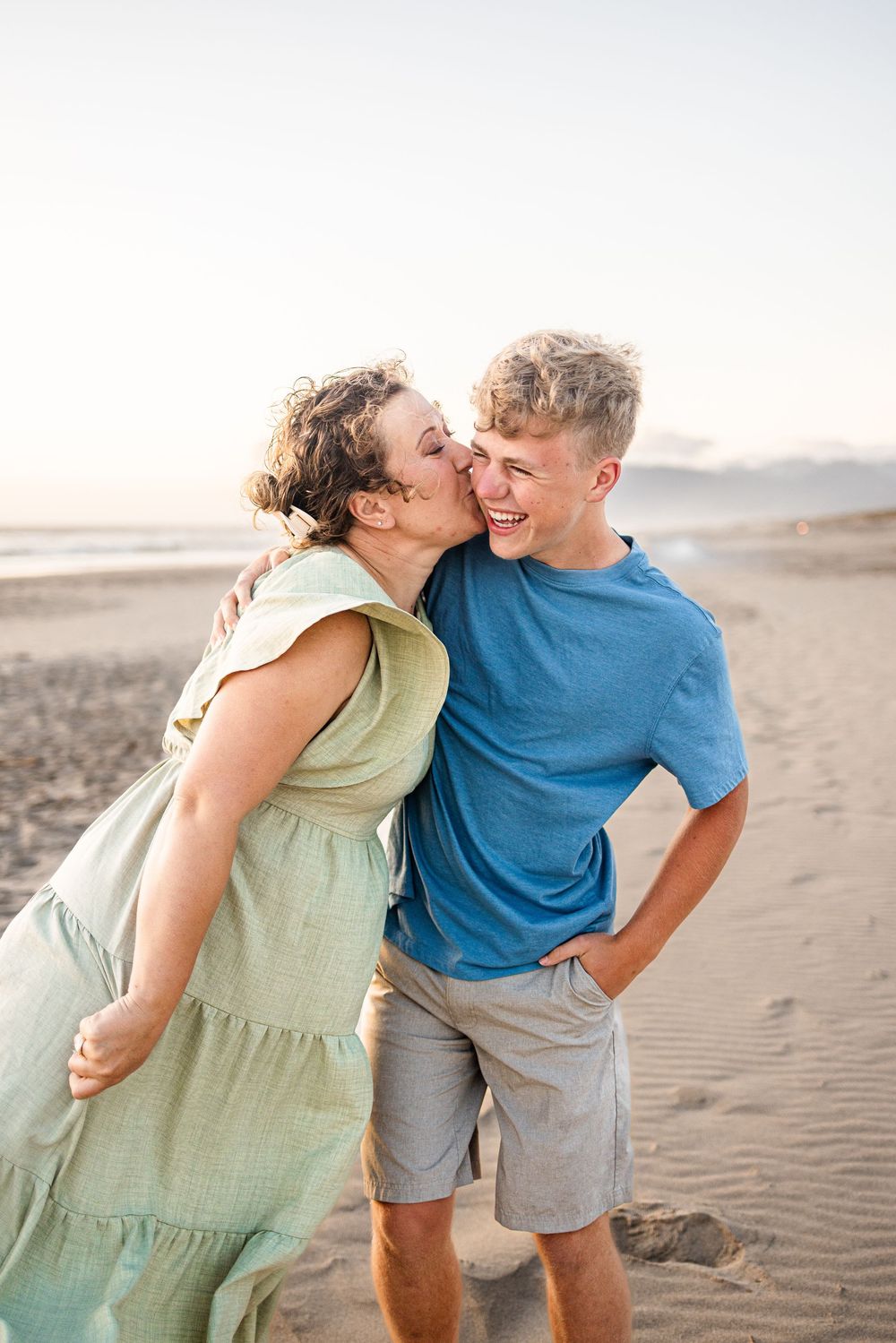 A couple shares romantic laughter and affection while walking together on a sandy beach at sunset.