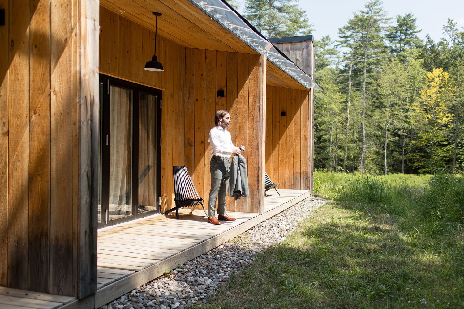Modern wooden cabin with covered porch surrounded by lush forest scenery on a sunny summer day.