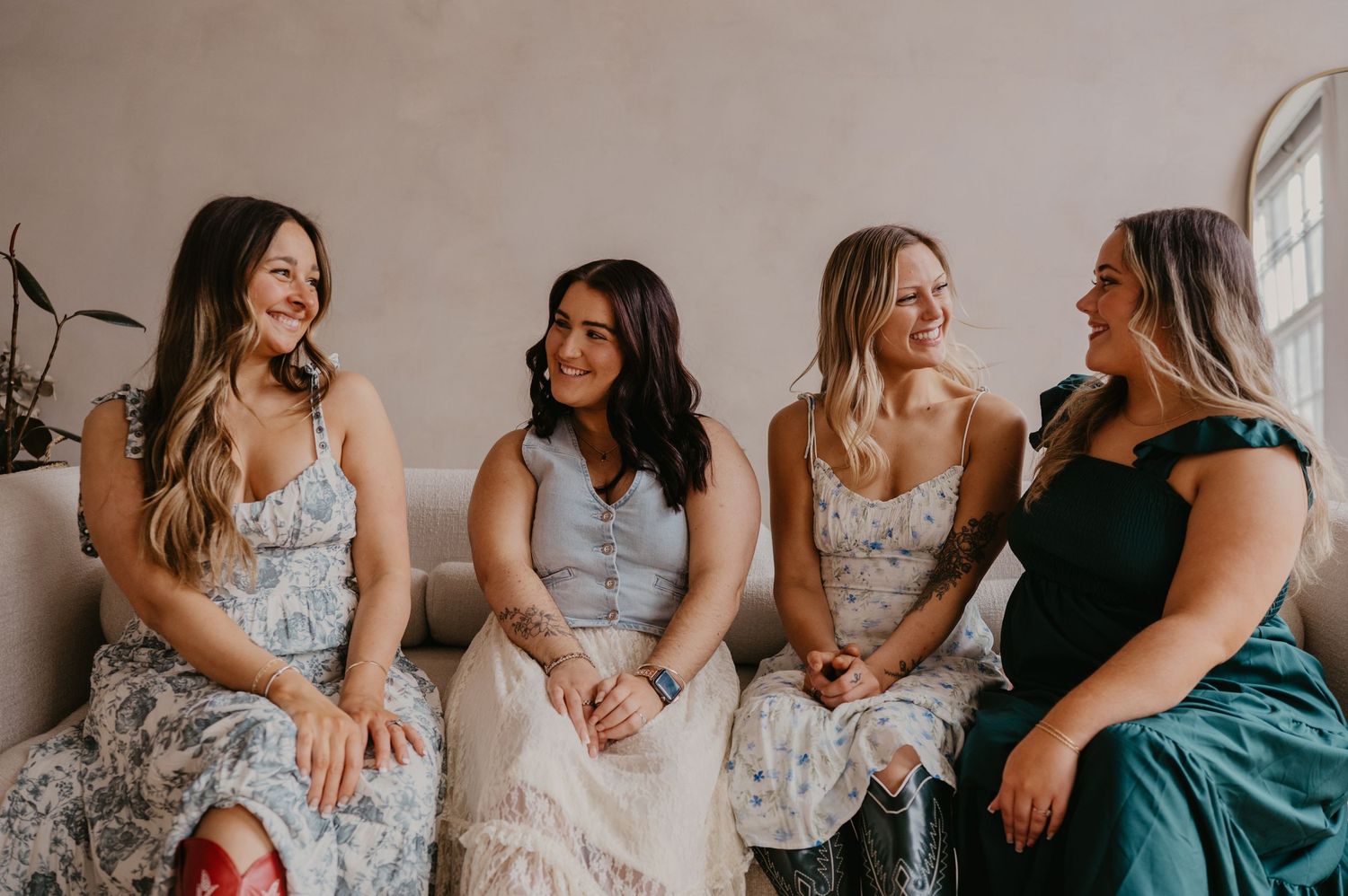 Four women in elegant dresses laughing together while seated, capturing a joyful bridal party moment.