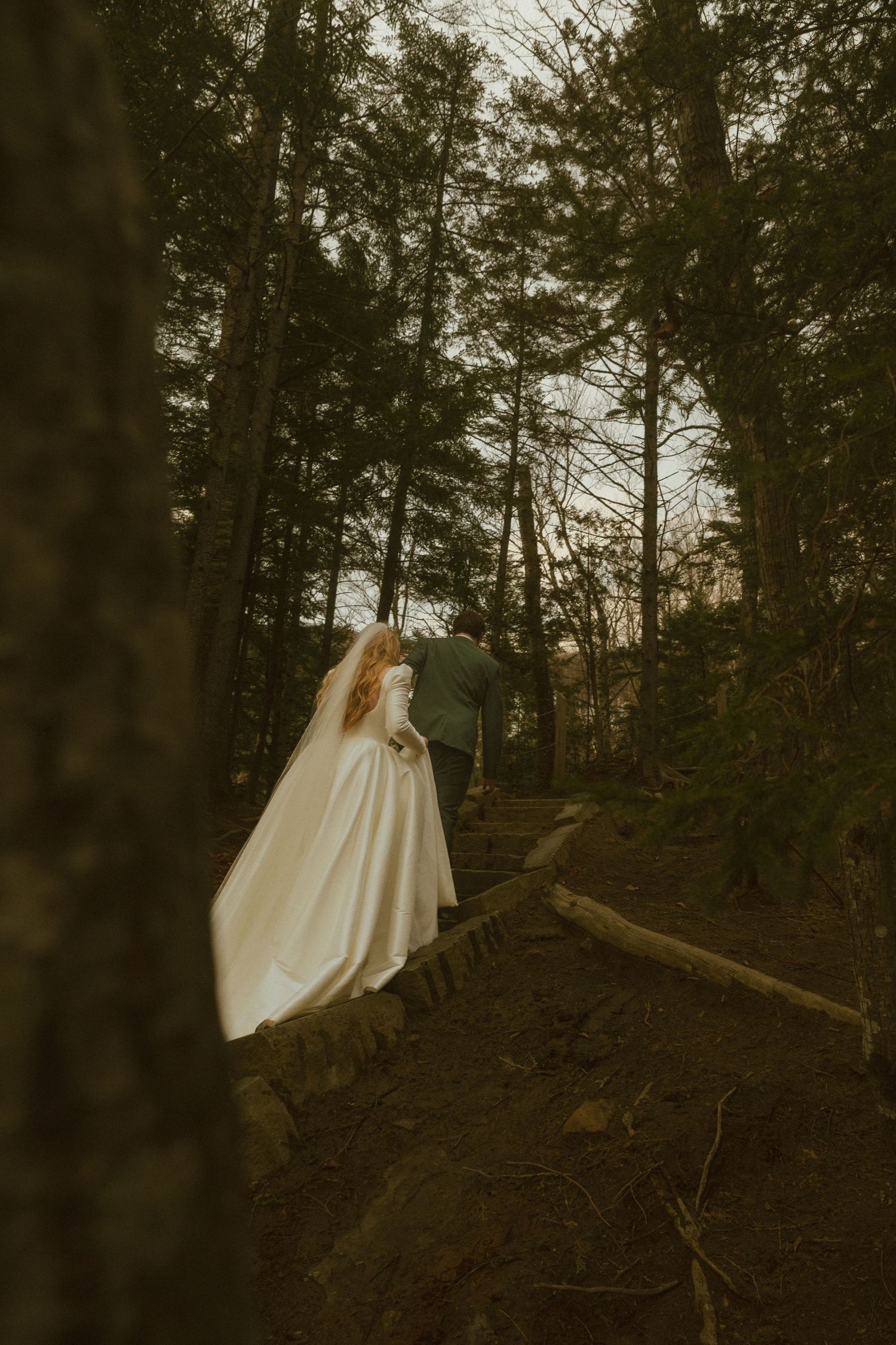 A person in a flowing white dress stands on a forest path at dusk.
