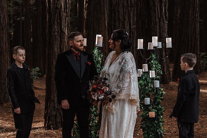 A wedding ceremony moment captured in a serene forest setting with towering trees and natural scenery.