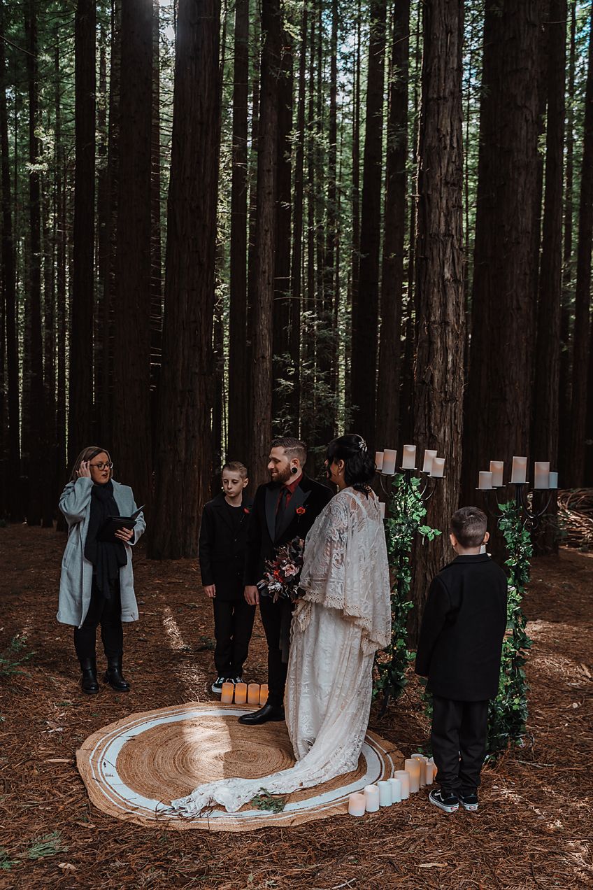 Intimate forest wedding ceremony surrounded by tall redwood trees showing guests and a long white wedding dress train.