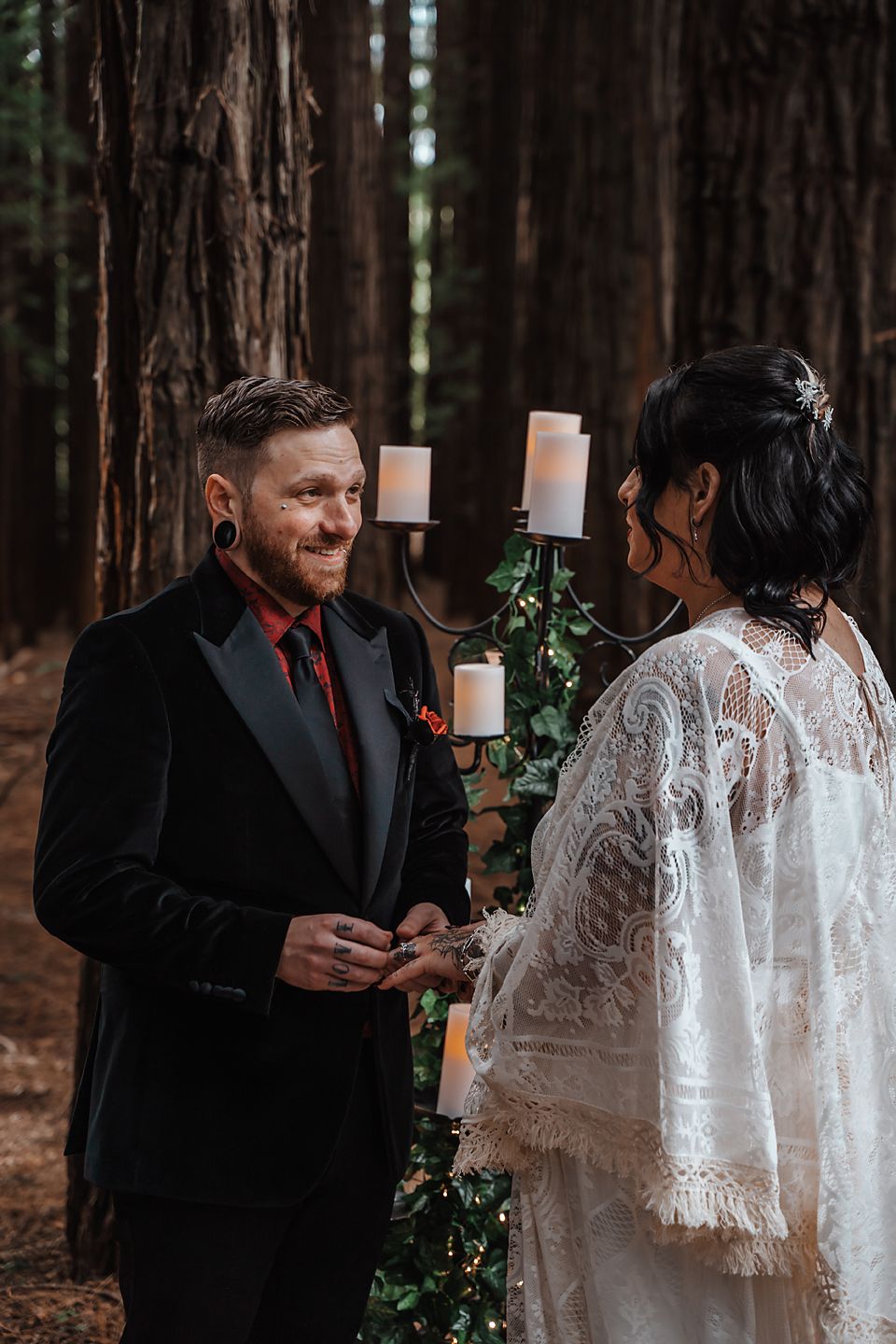 A romantic wedding couple shares intimate moments in a forest setting with white candles and lace details.