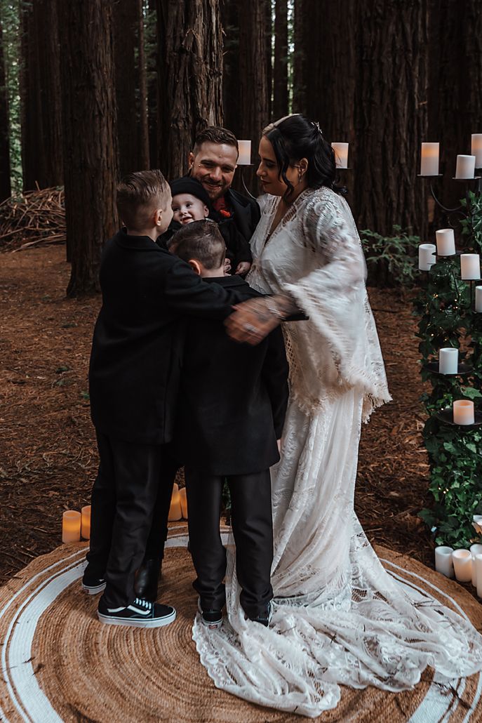 A heartwarming moment during a forest wedding ceremony as a family embraces on a circular rug surrounded by candles.