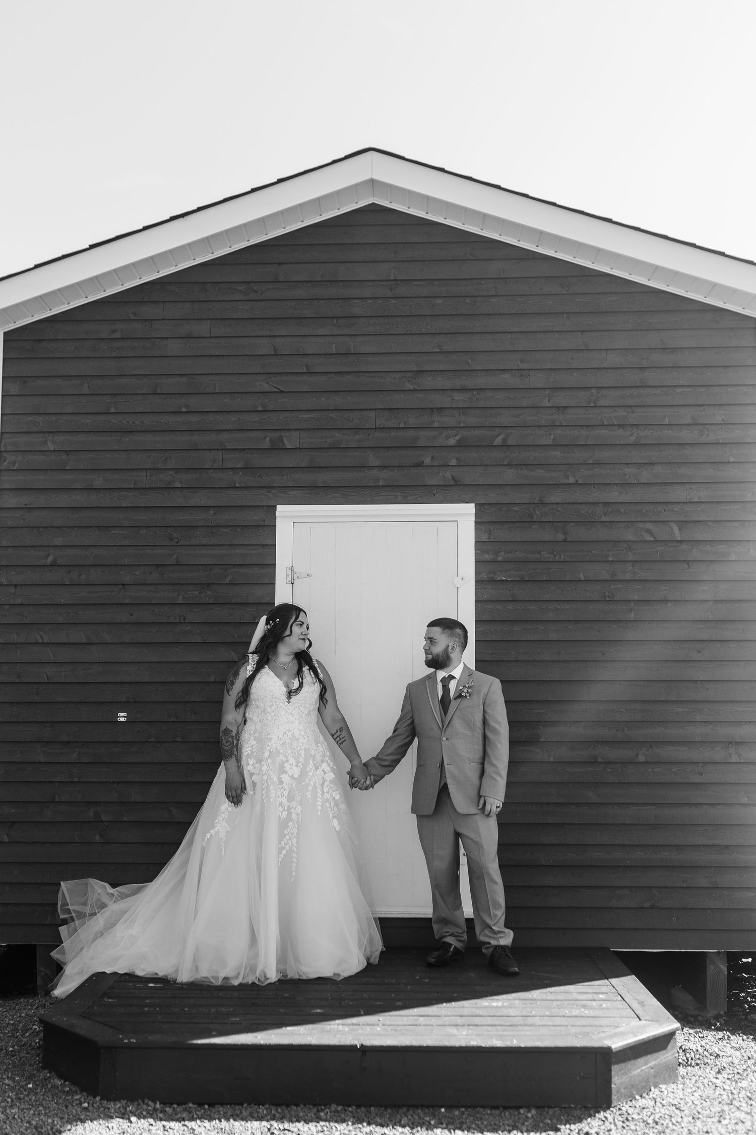 Wedding couple in formal attire pose against row of black wooden buildings creating dramatic contrast.