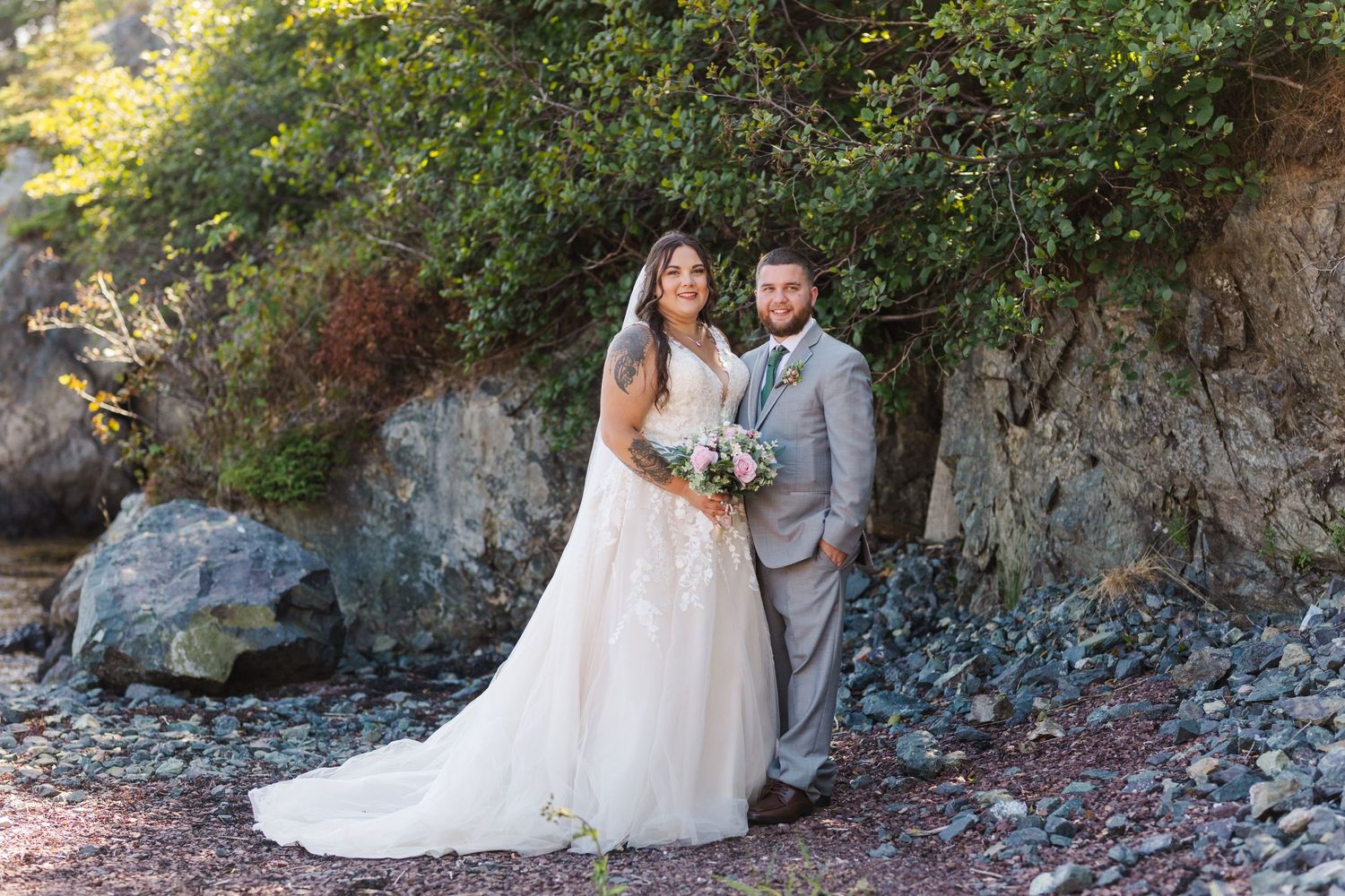 A couple in wedding attire poses together on a rustic path against a rocky cliff backdrop during autumn.