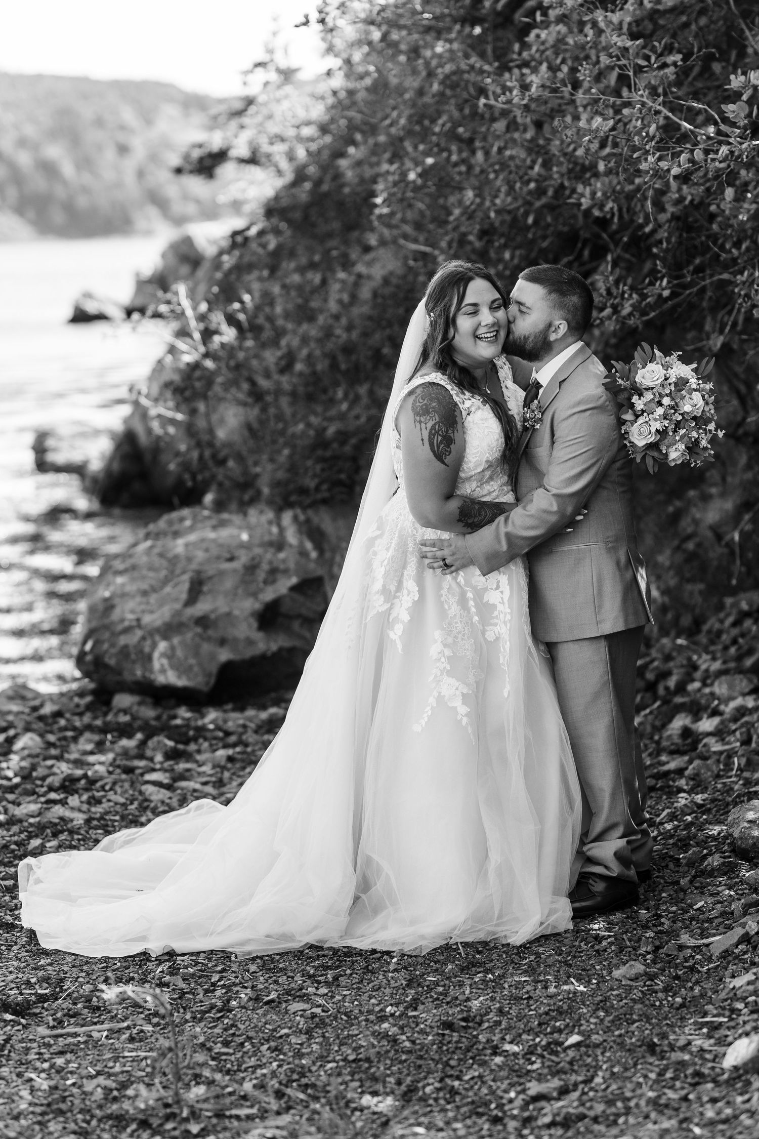 A romantic black and white wedding photo series showing a couple sitting together on rocks by a scenic coastline.
