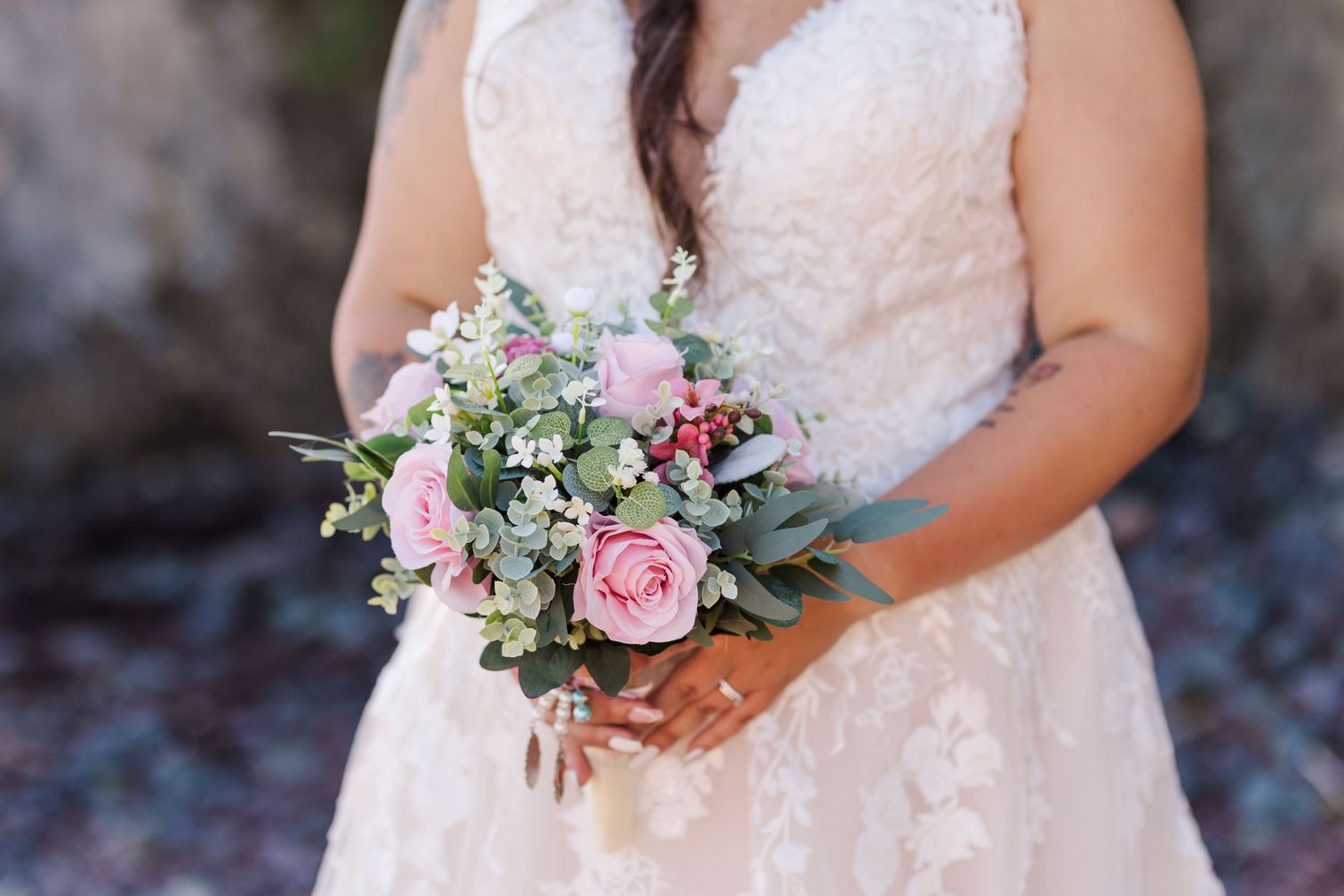 Close-up of wedding bouquet with pink roses and eucalyptus held against white lace wedding dress.