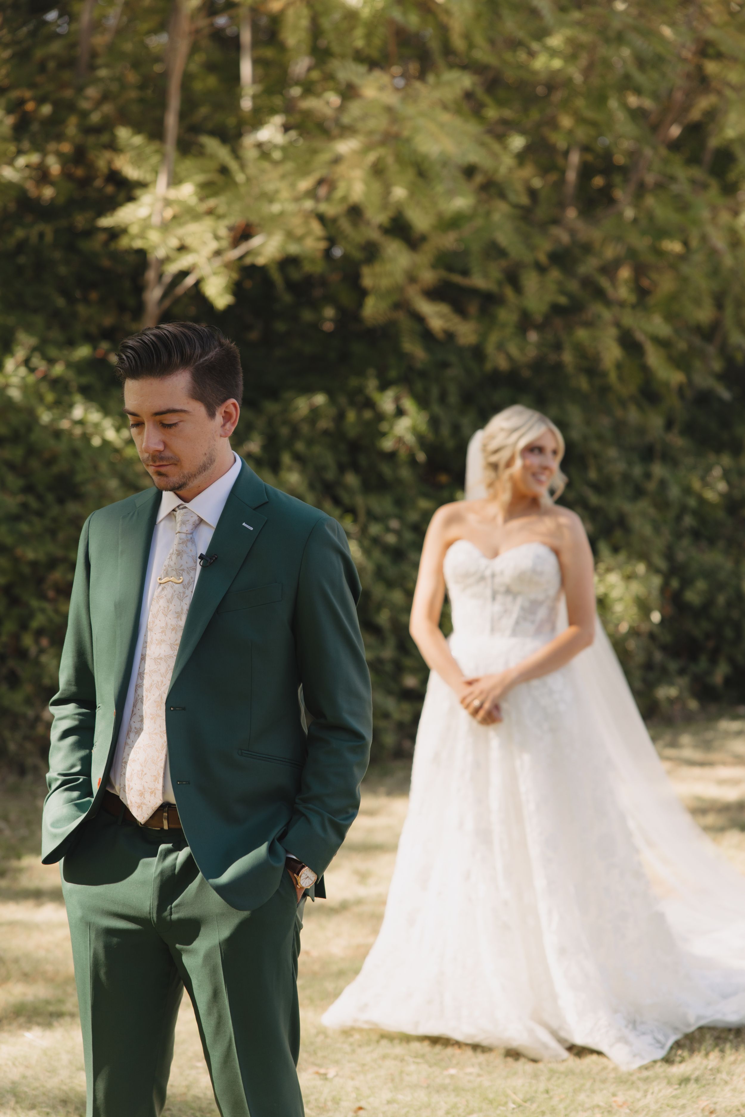 First look wedding photography series showing couple in white dress and emerald green suit in outdoor garden setting.
