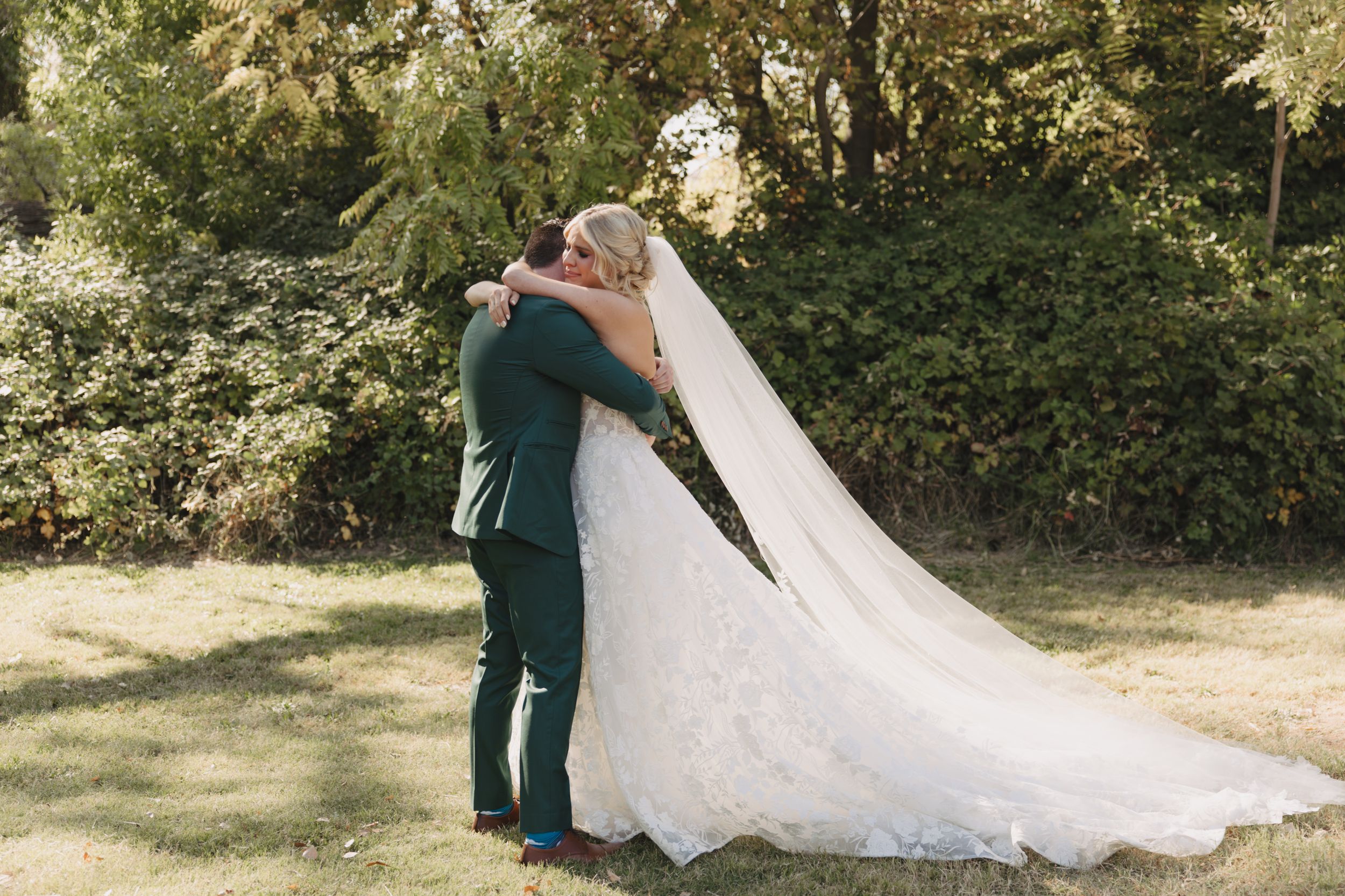 A couple in wedding attire shares an intimate moment in a sun-dappled garden setting.