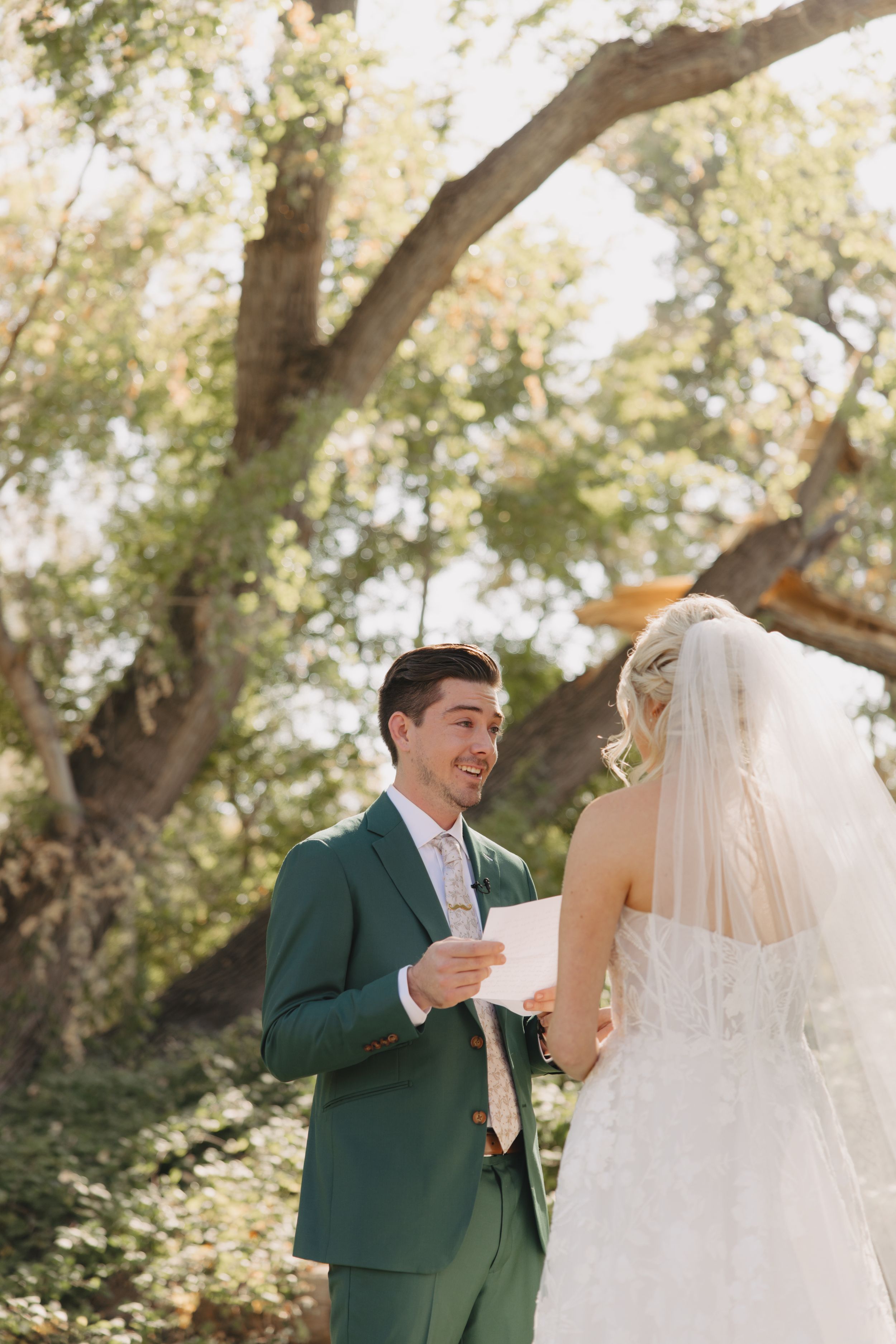 A couple shares an intimate first look moment in an outdoor wedding setting with sunlit trees in the background.