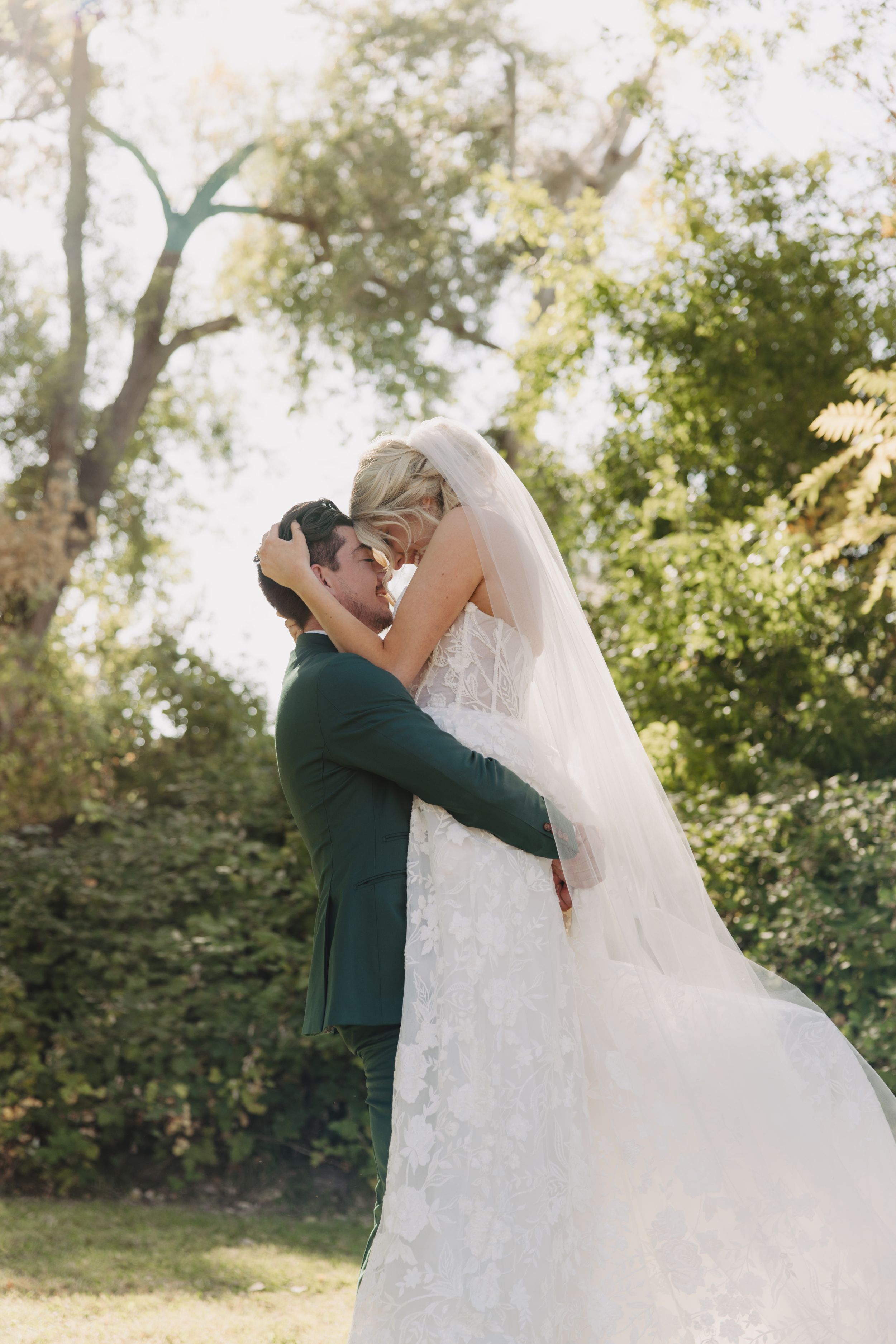A couple shares a romantic moment during their wedding photoshoot in a sun-drenched garden setting.