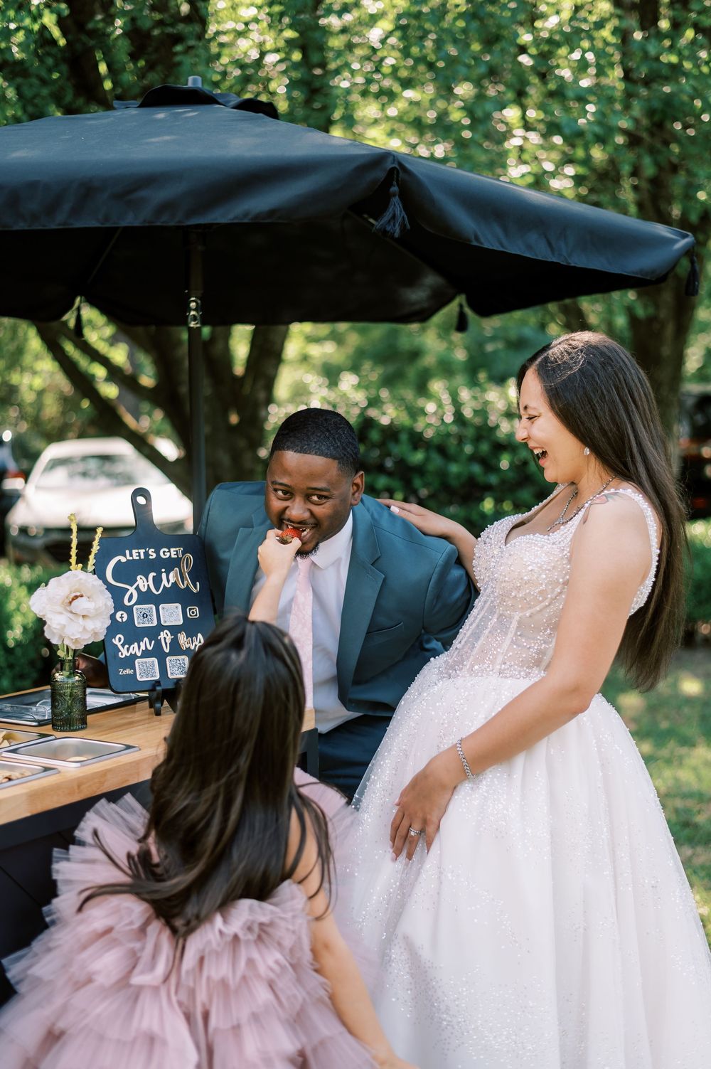 Guests laughing and celebrating at an outdoor wedding reception with decorative black bar setup.