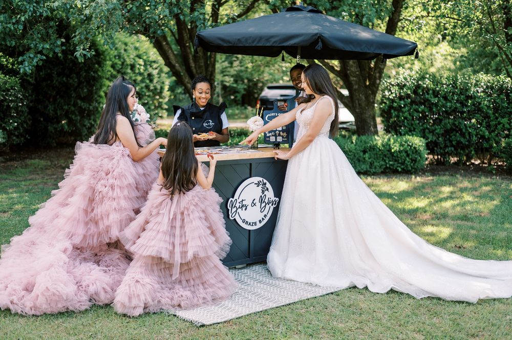 Wedding celebration scene outdoors featuring a black mobile bar station with pink and white decor elements.