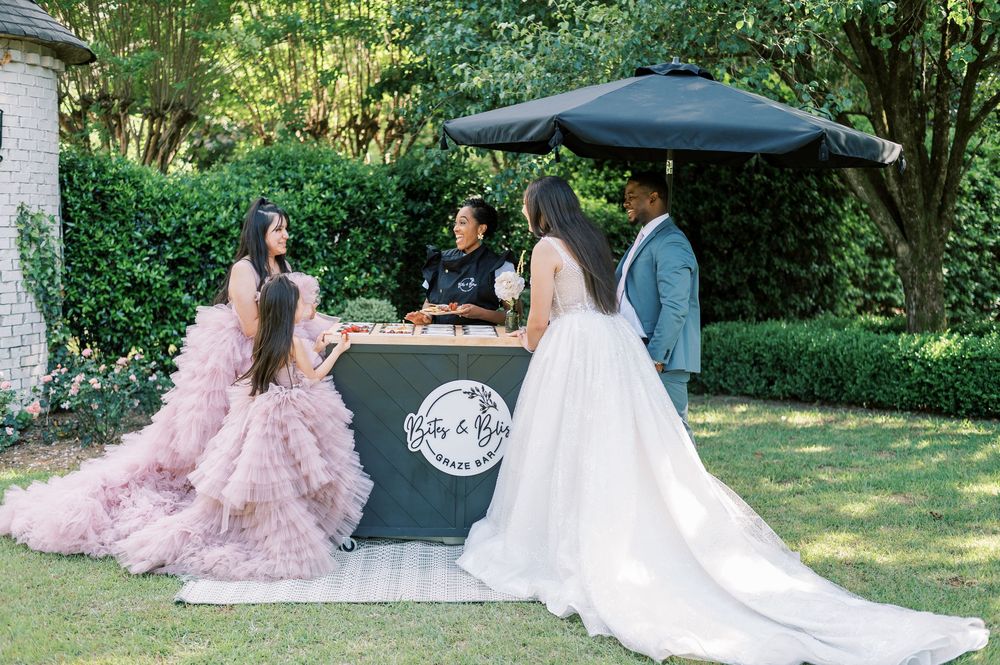 People in formal attire enjoying a sunny outdoor gathering with white dresses and pink gowns.