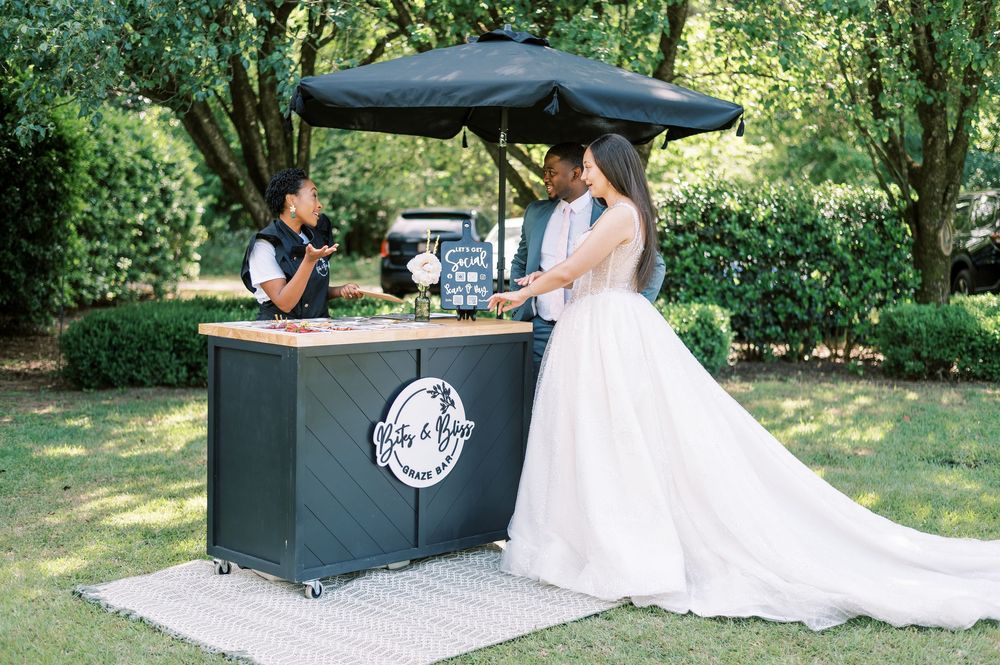 A catering station with food service trays set up outdoors against a white brick wall in a garden setting.