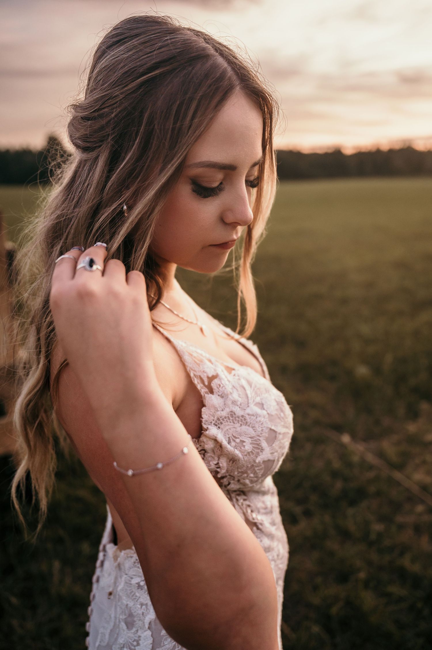 A bride in a lace wedding dress poses in a field at sunset in a series of romantic portraits.