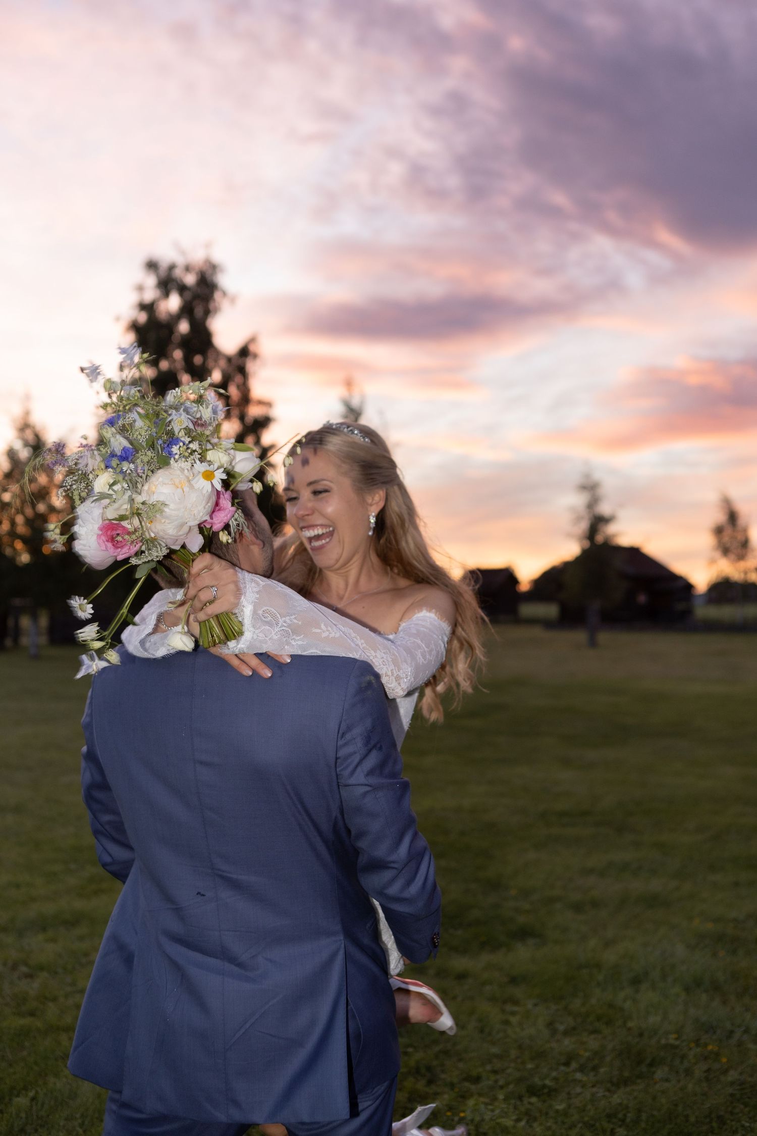 Couple in white attire sharing an intimate moment on a tree-lined path.