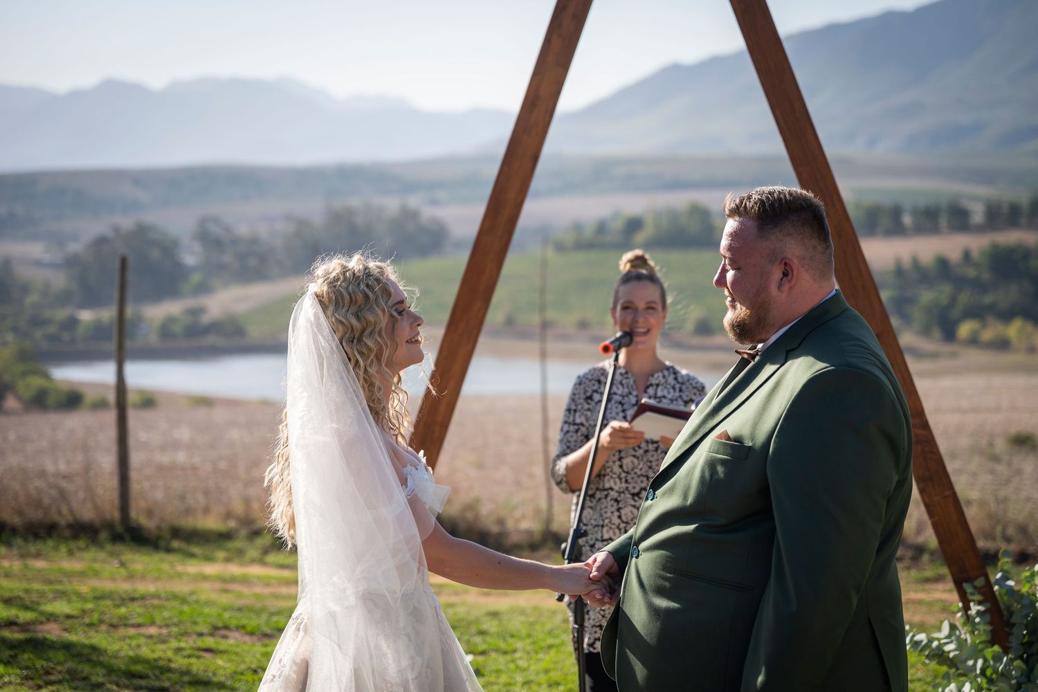 Outdoor wedding ceremony with beautiful mountain landscape backdrop on grassy hillside under wooden arch structure.