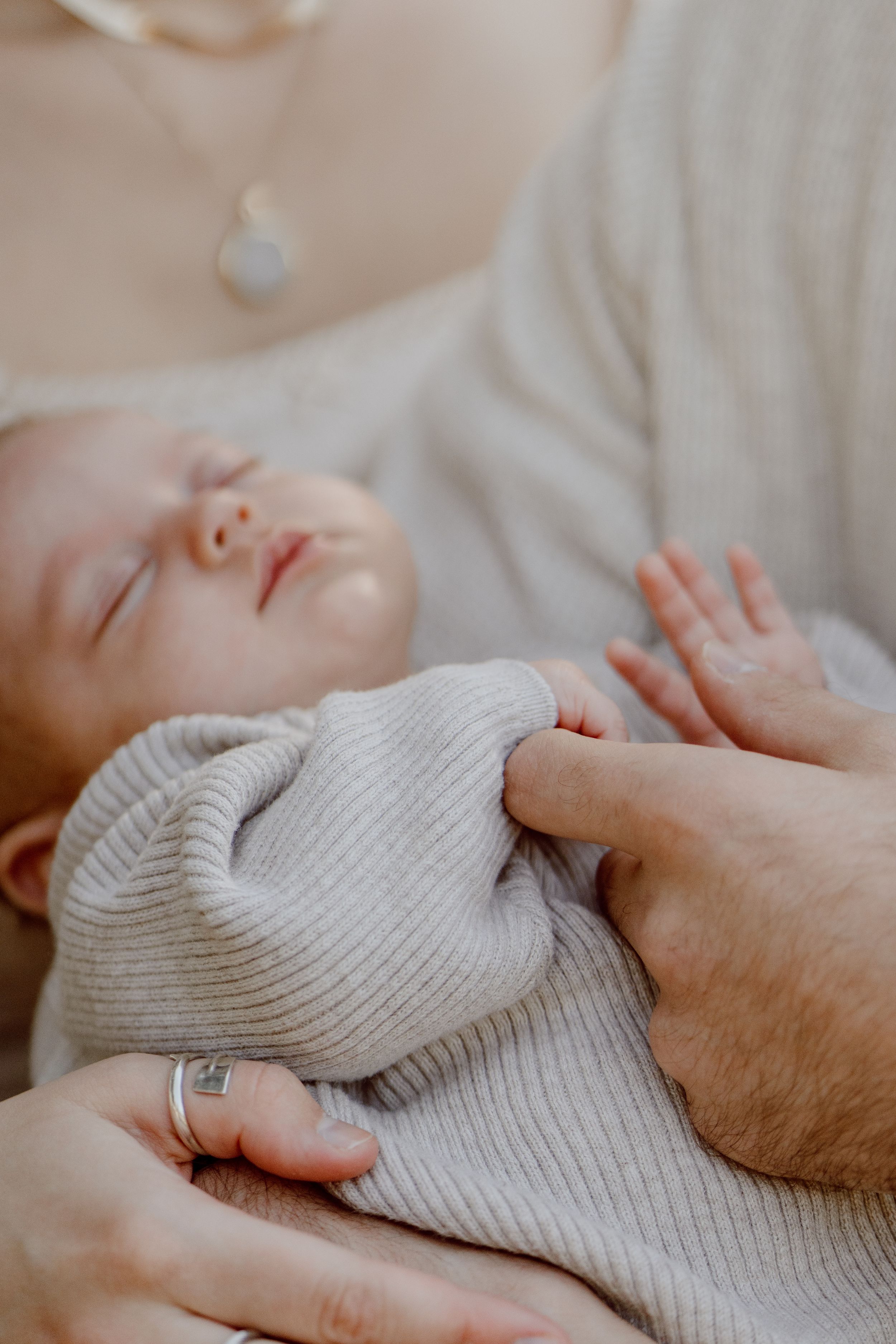 A sleeping infant in a ribbed white sweater rests peacefully while being held.
