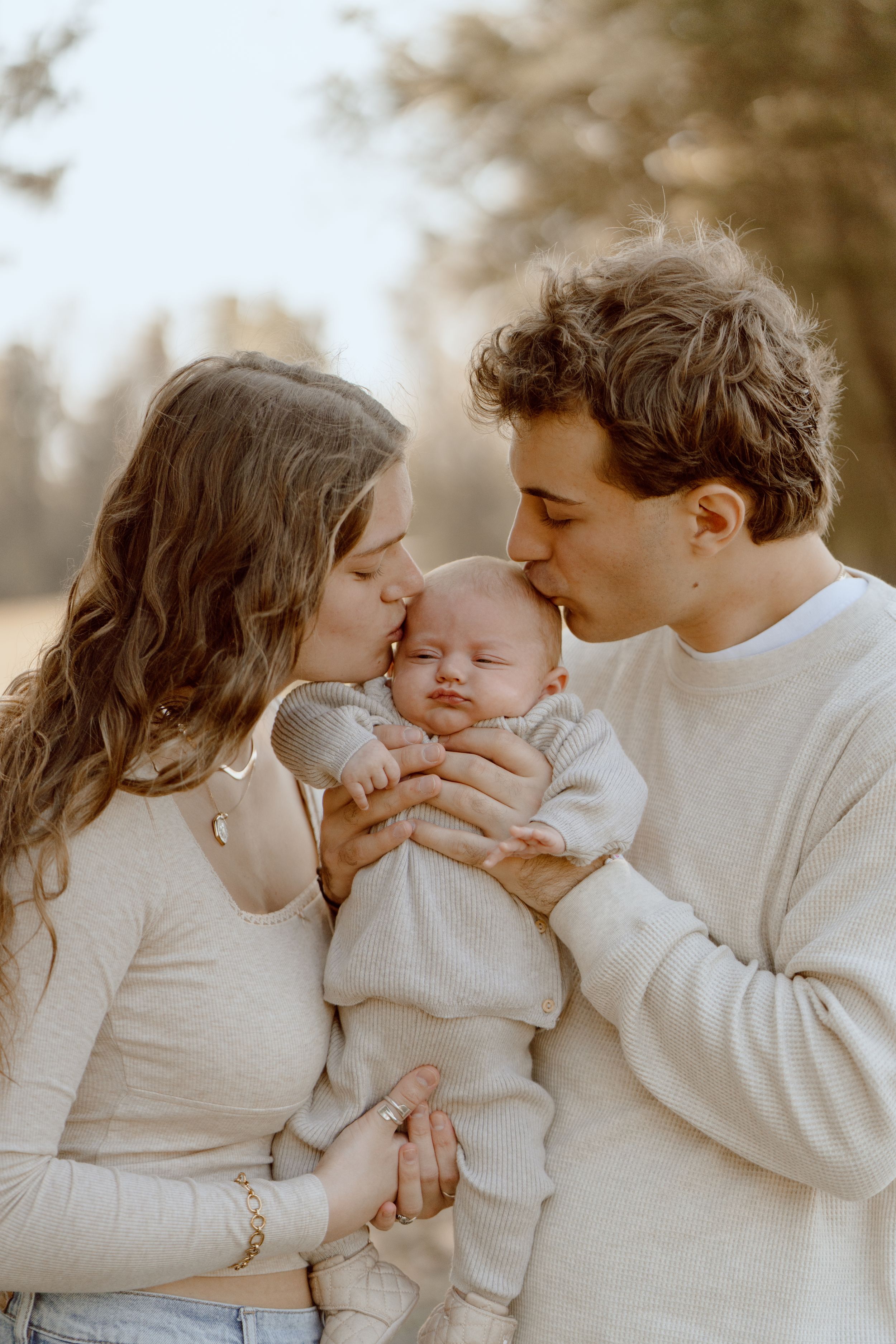 Parents sharing an intimate moment with their baby outdoors in matching cream sweaters.