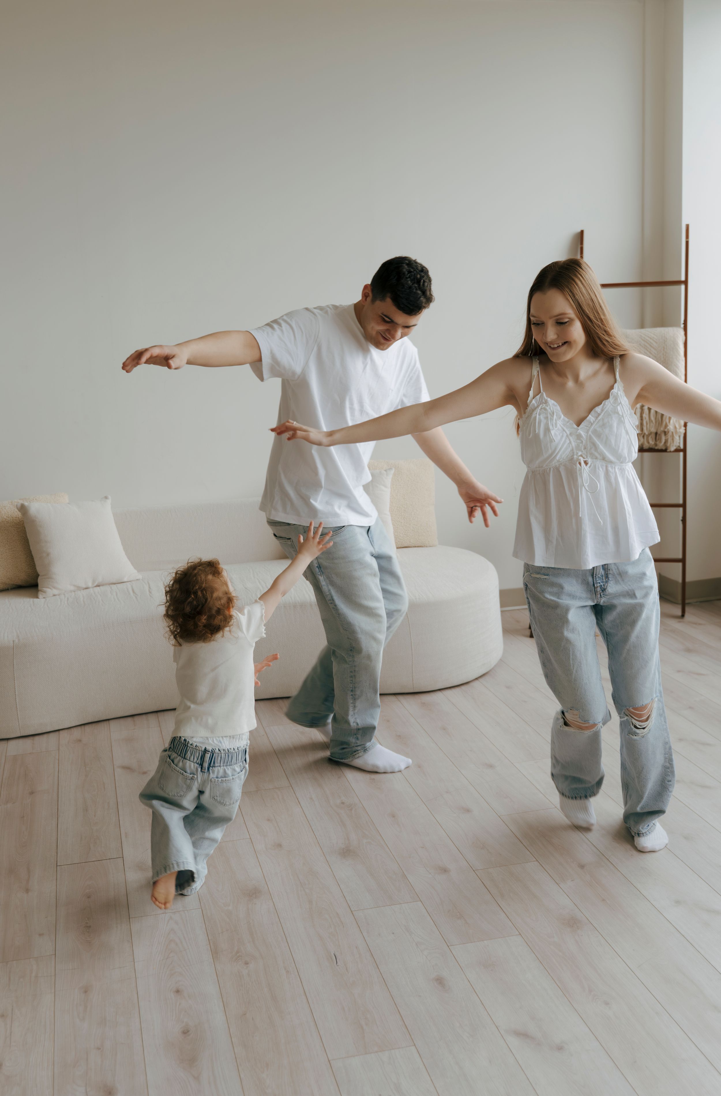 A happy young family dancing and playing together in a bright modern living room with hardwood floors.