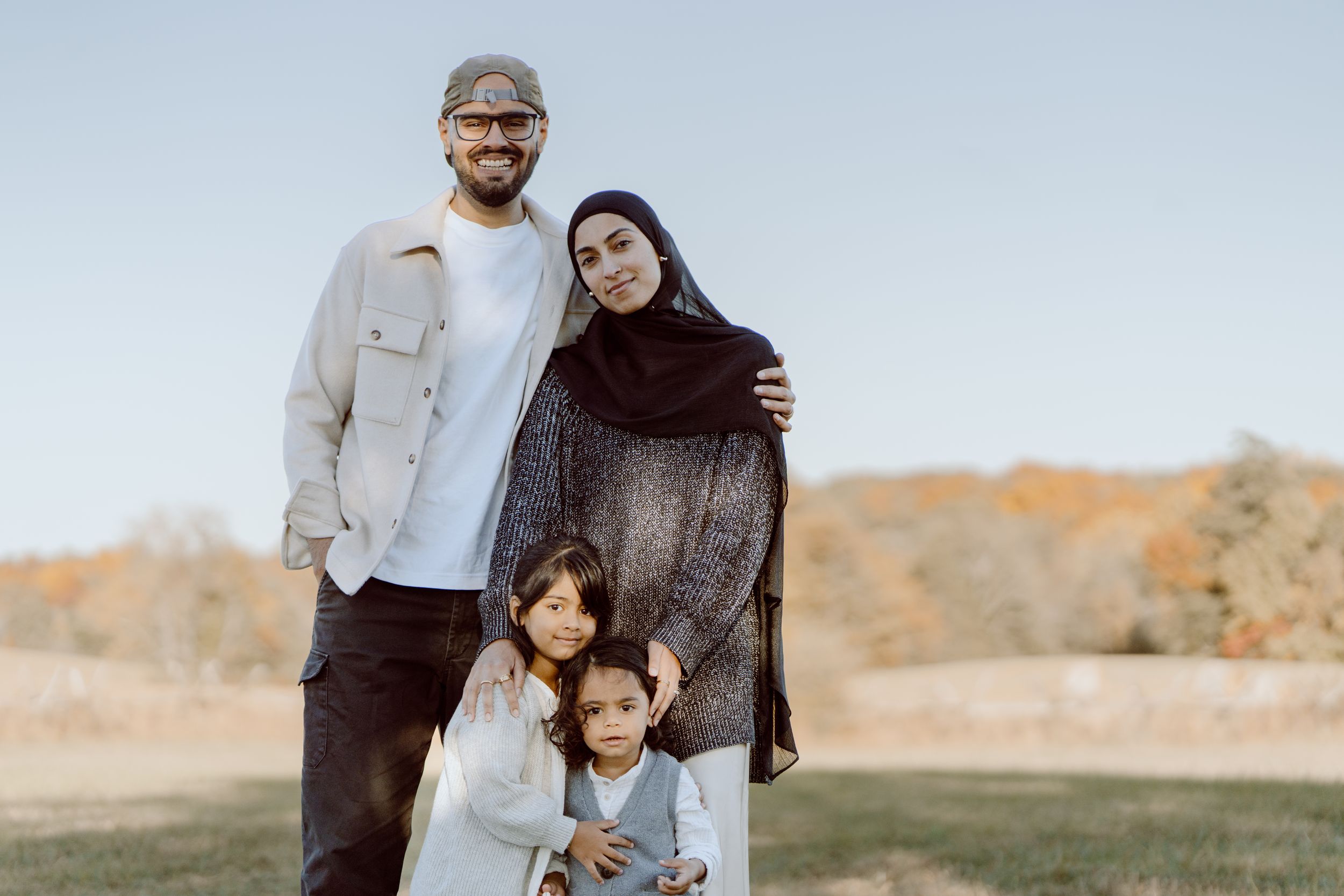 A family poses together outdoors against a light background.