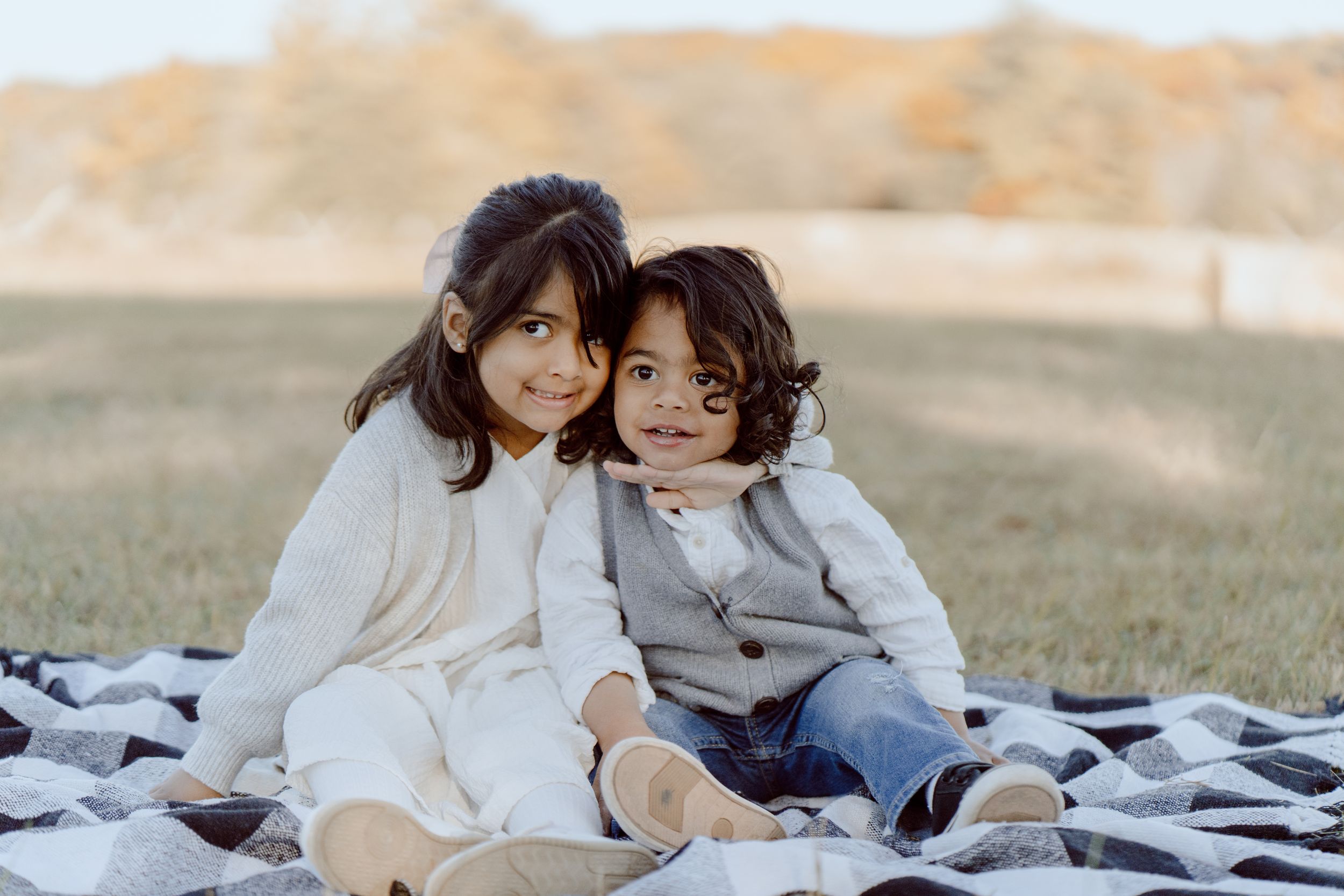 A loving scene captured during an outdoor family photoshoot in warm sunlight on a blanket in the grass.