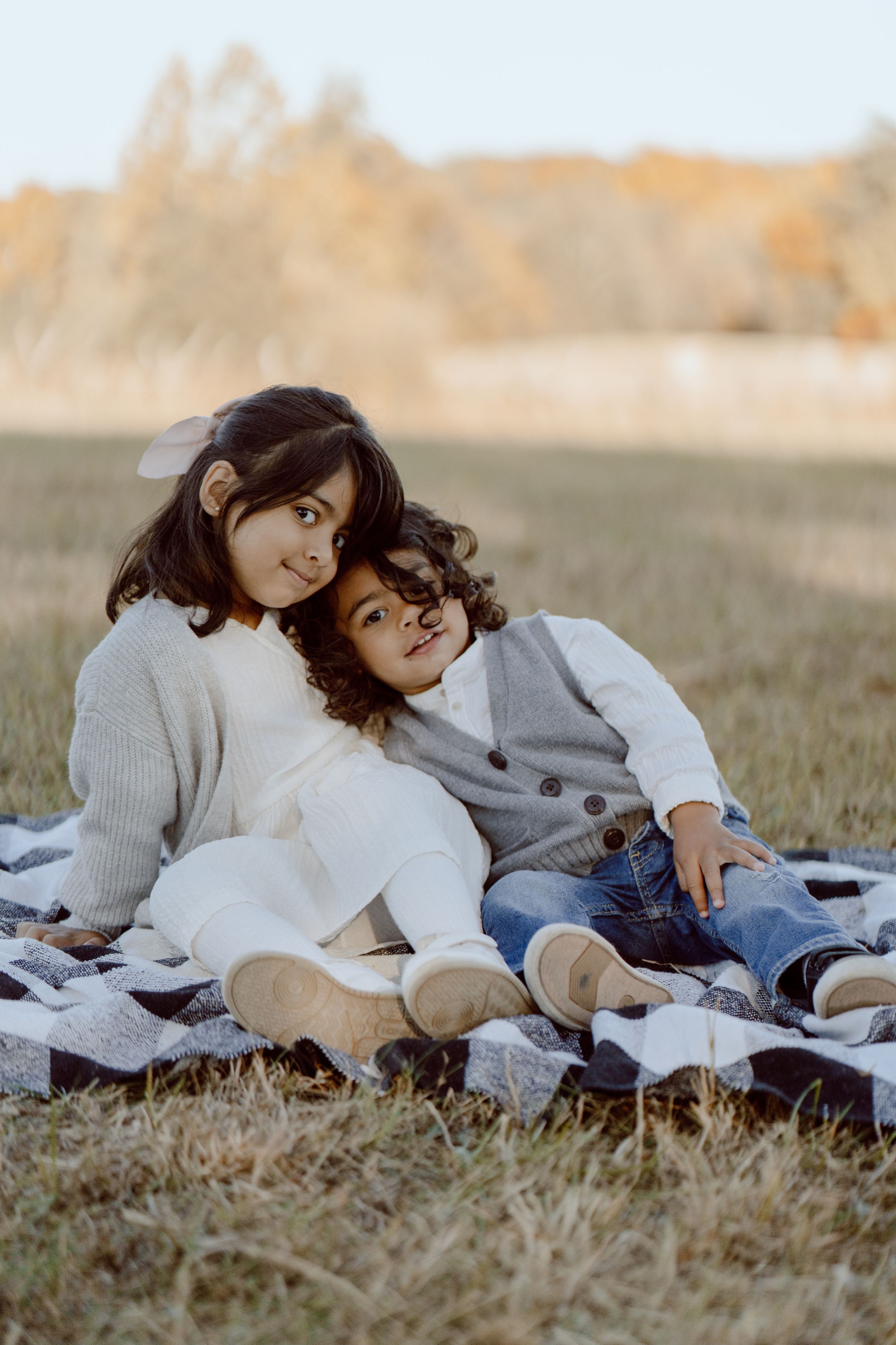 Tender outdoor photoshoot scene with cozy sweaters and natural lighting on a grassy field.
