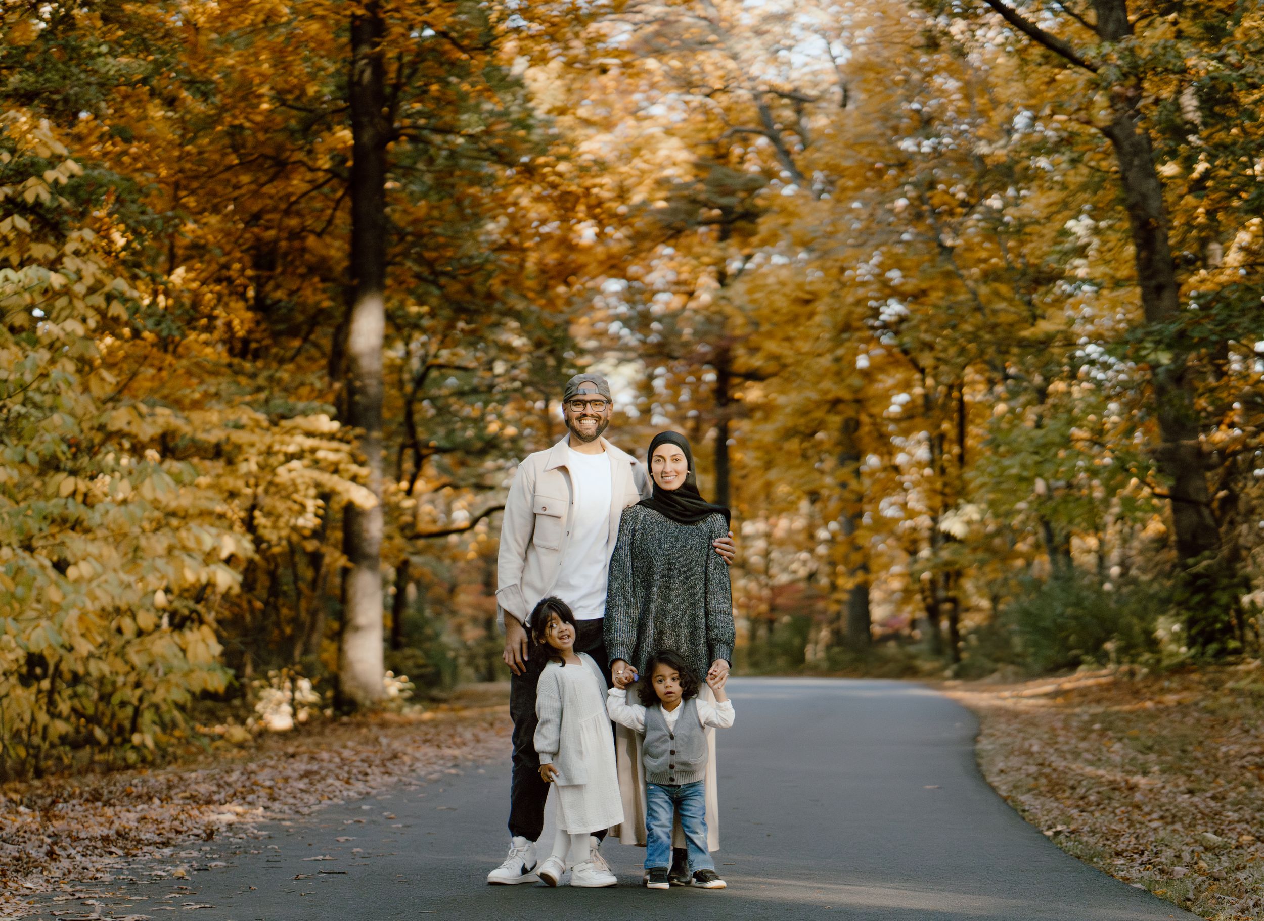 Family walking along a tree-lined autumn path with golden foliage overhead.
