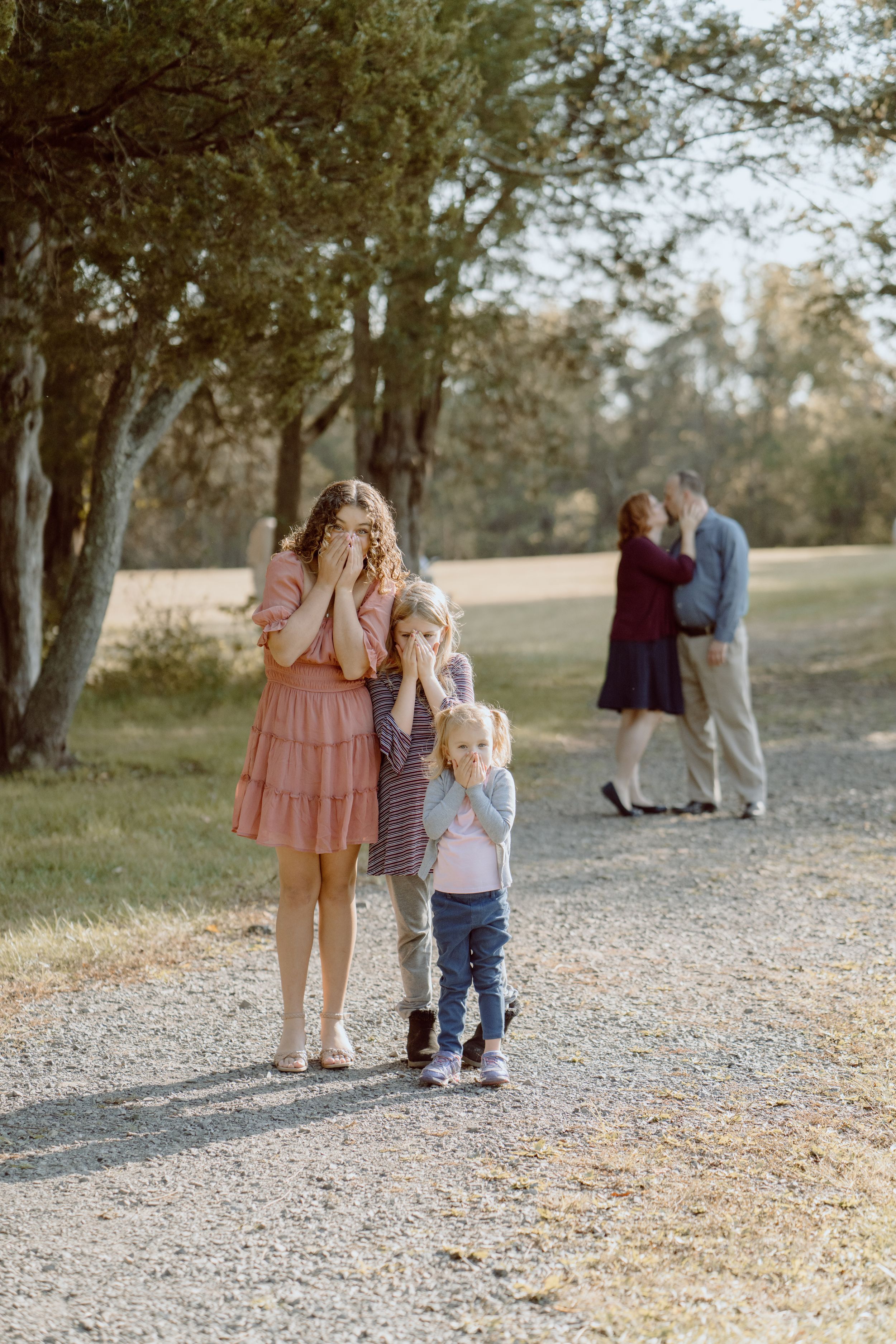 Casual family photo session on a winding gravel path surrounded by trees.