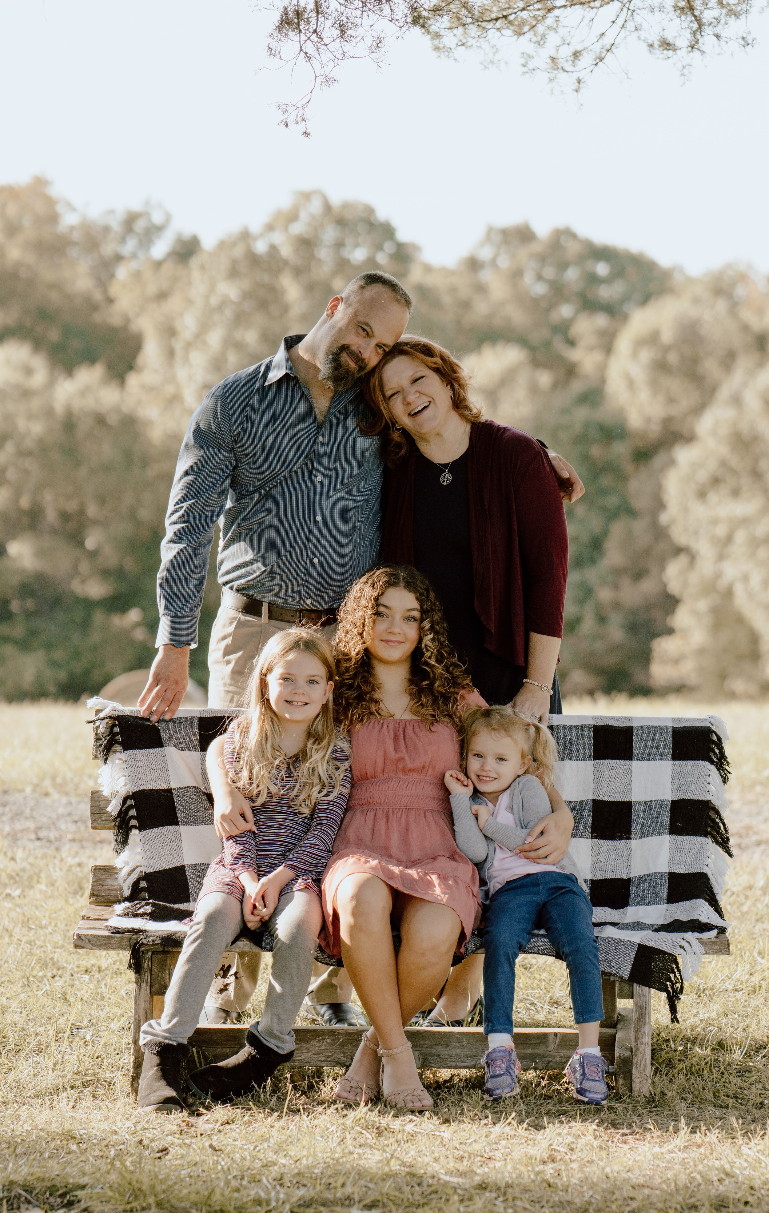 Family relaxing together on a black and white checkered blanket during an outdoor photoshoot.