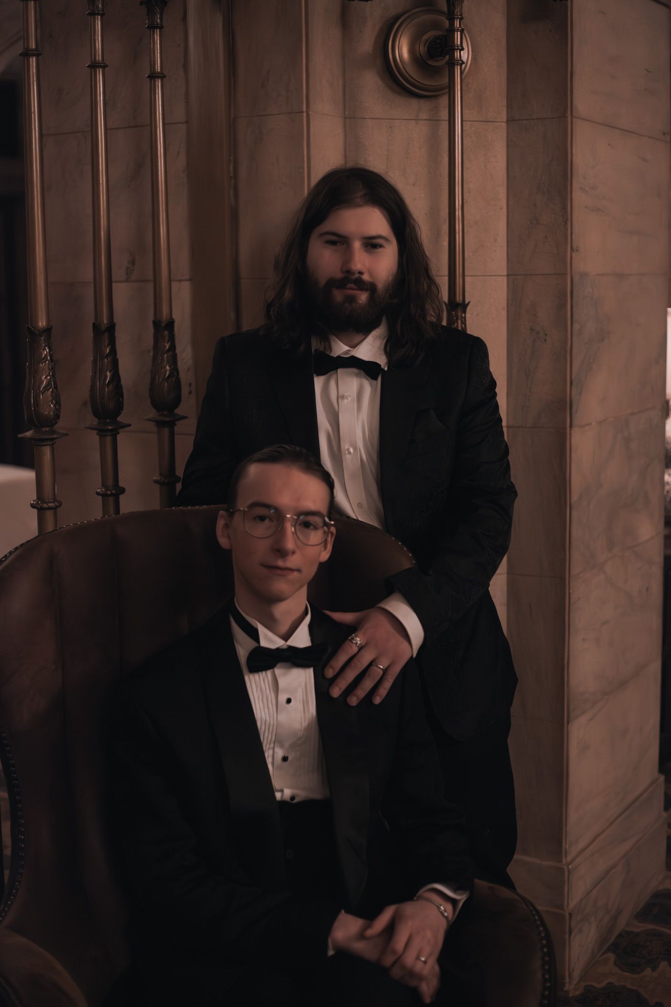 Two people in formal attire pose dramatically on vintage wooden stairs.