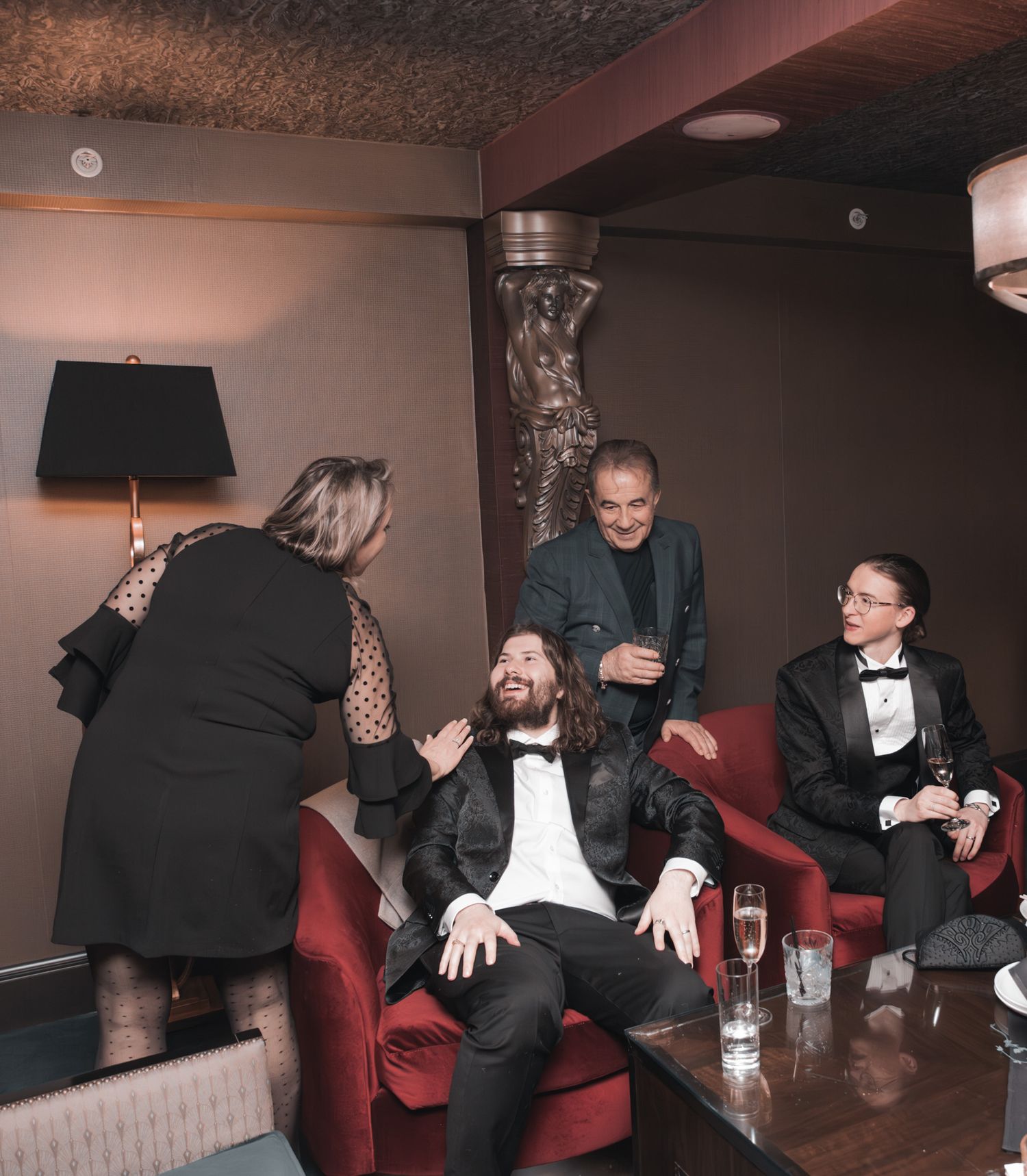 A group enjoying drinks and conversation on a red couch in a dimly lit lounge setting.