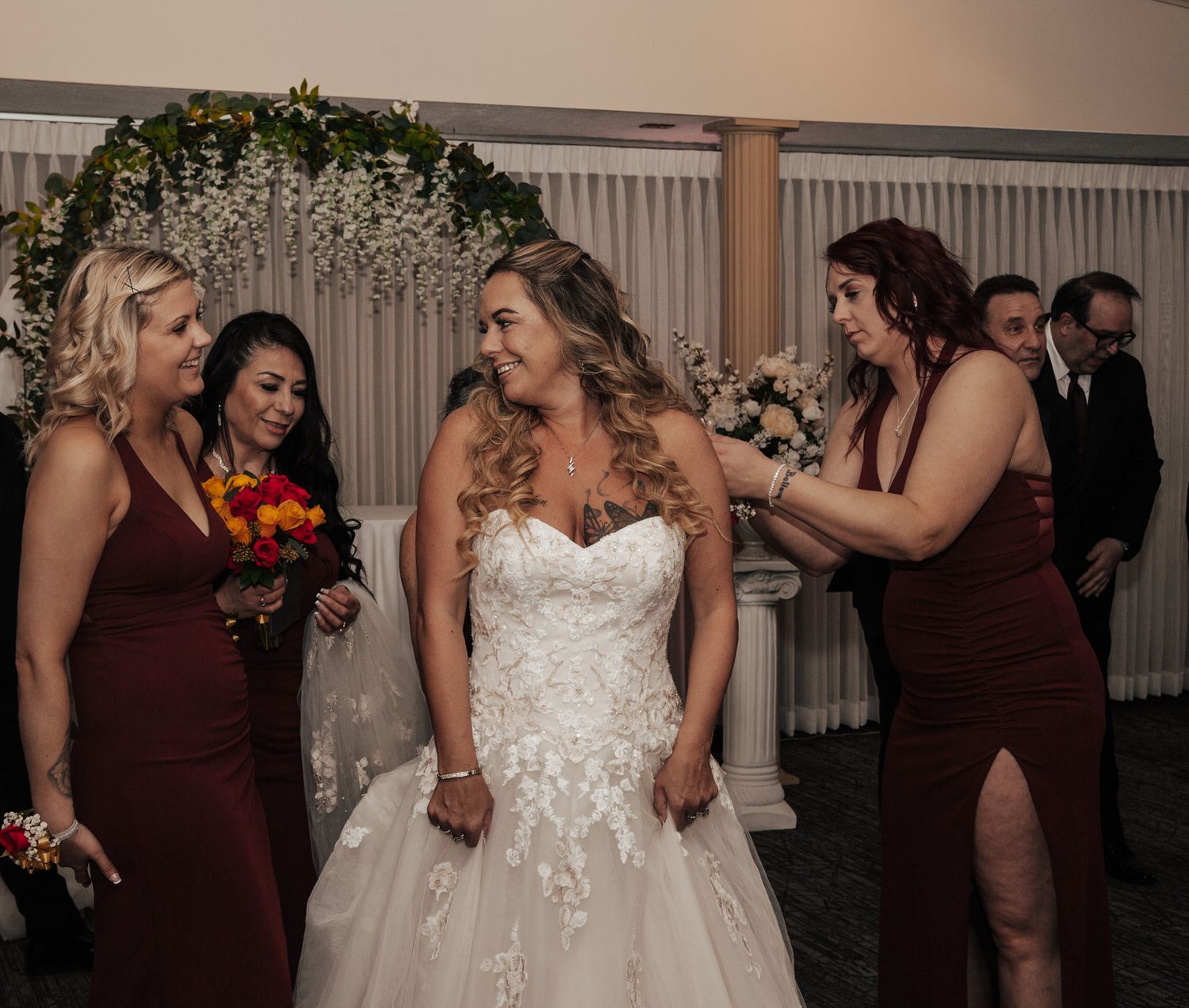 Bridesmaids in burgundy dresses celebrate with the bride in a decorated reception venue.