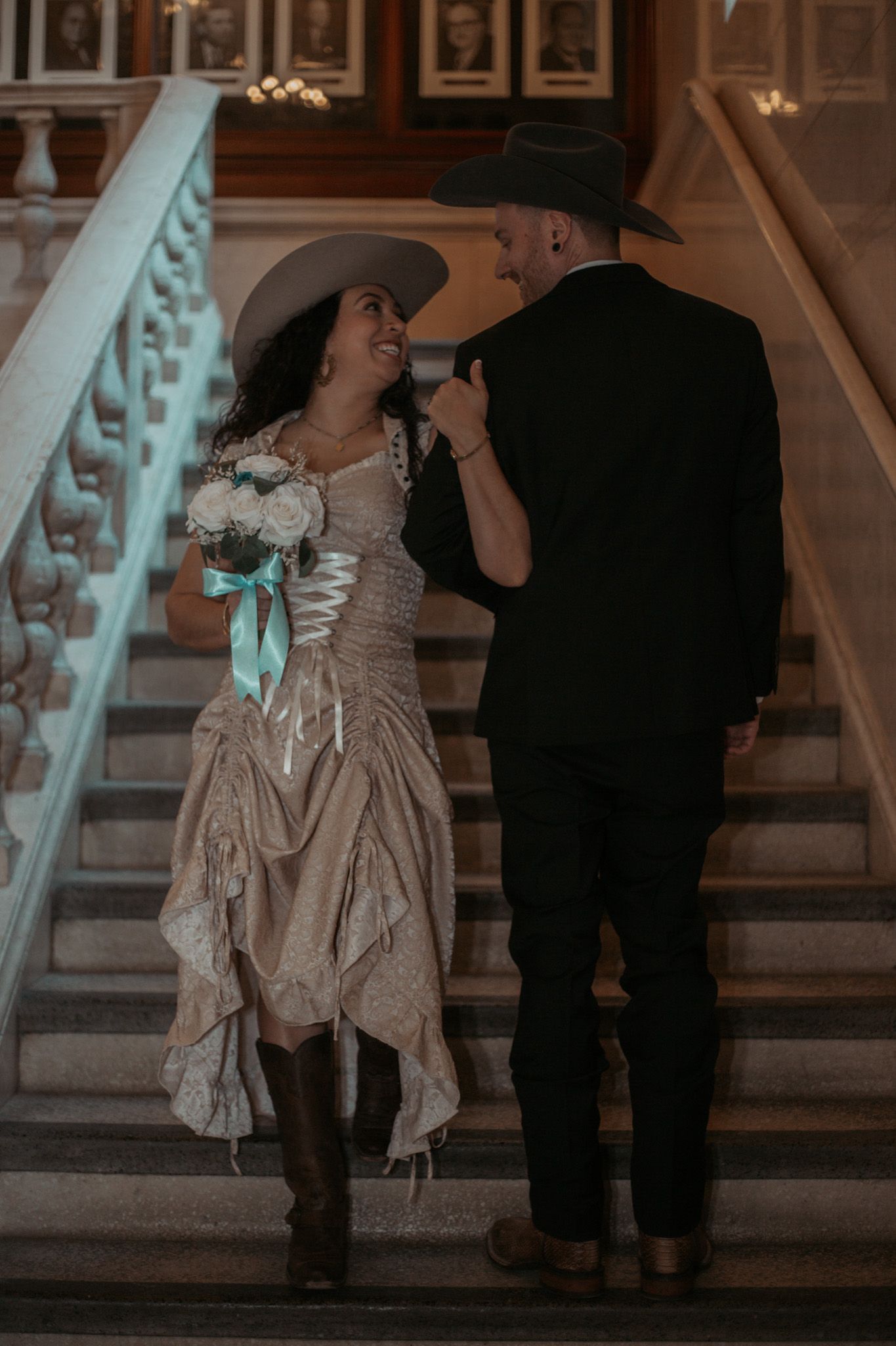 A couple in vintage-inspired wedding attire share a moment on an elegant staircase.