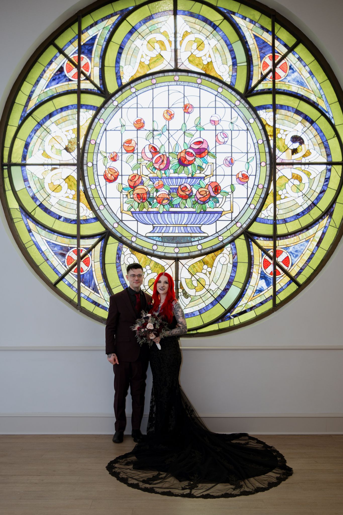 Artistic portraits taken in front of a colorful stained glass window with floral designs.