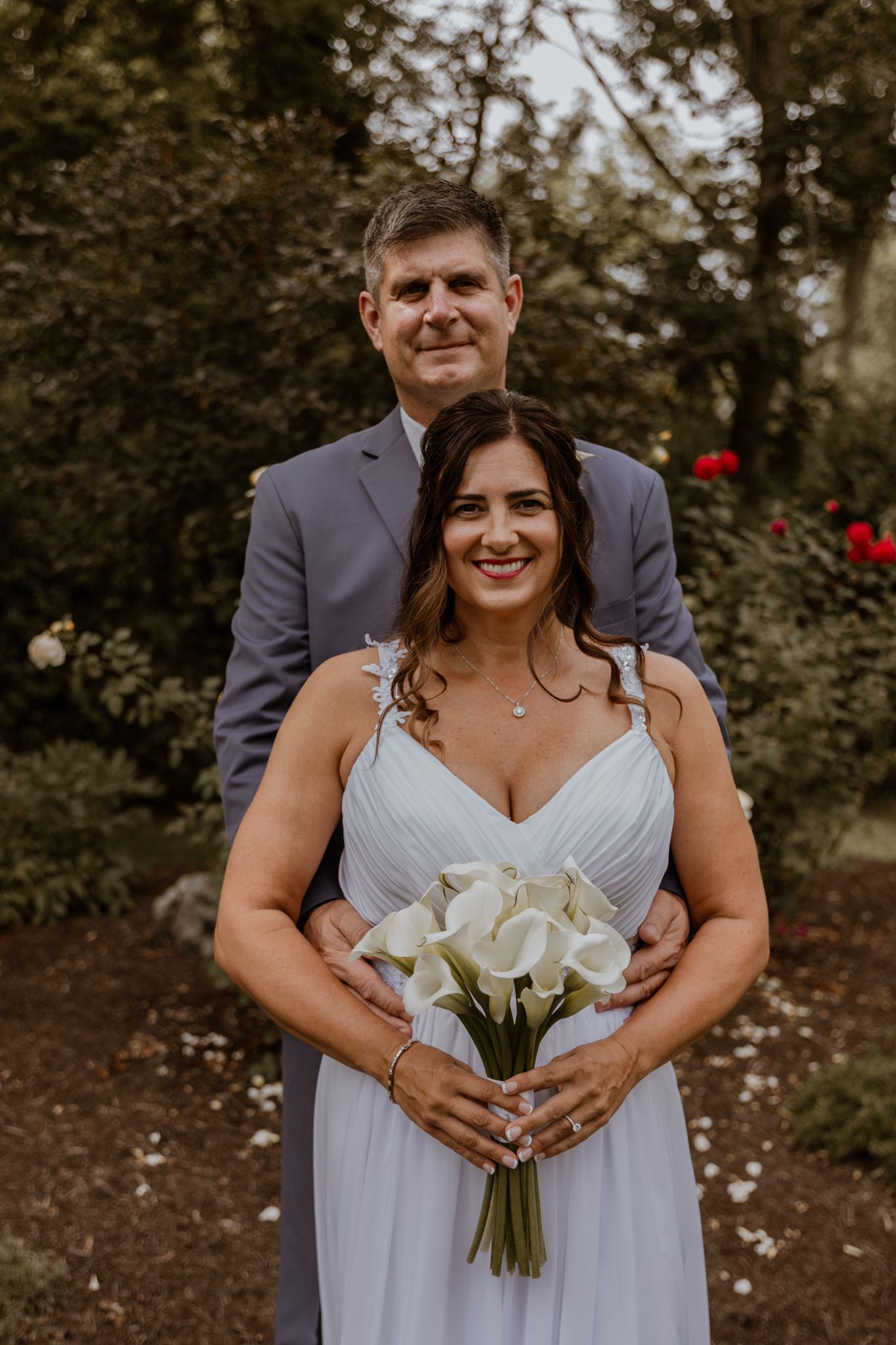 A bride in white holds a bouquet of calla lilies during an outdoor photo session.