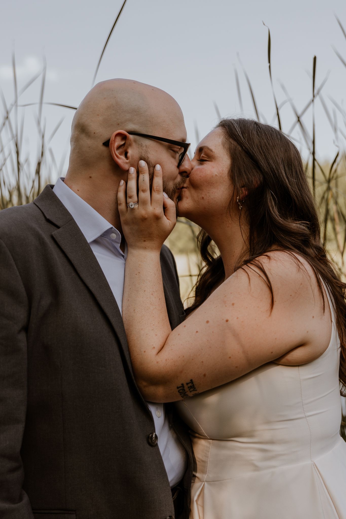 A romantic kiss between newlyweds against a natural outdoor backdrop.